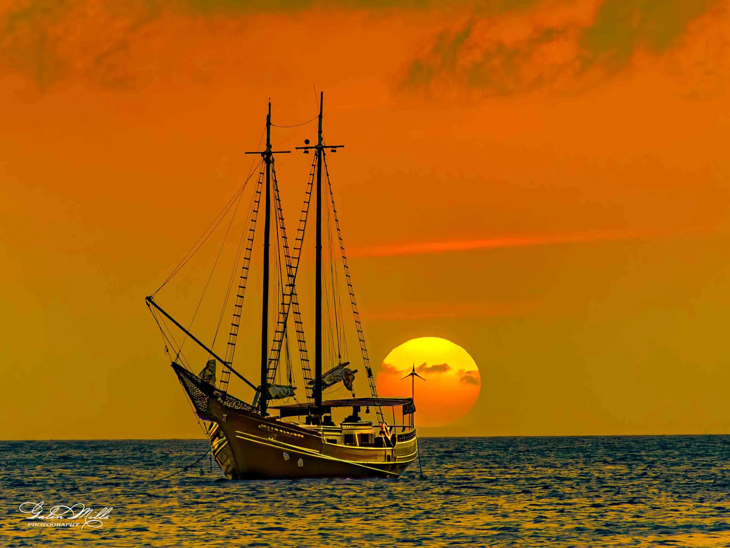 A silhouette of a sailing ship on the ocean during sunset with the sun near the horizon and orange sky.
