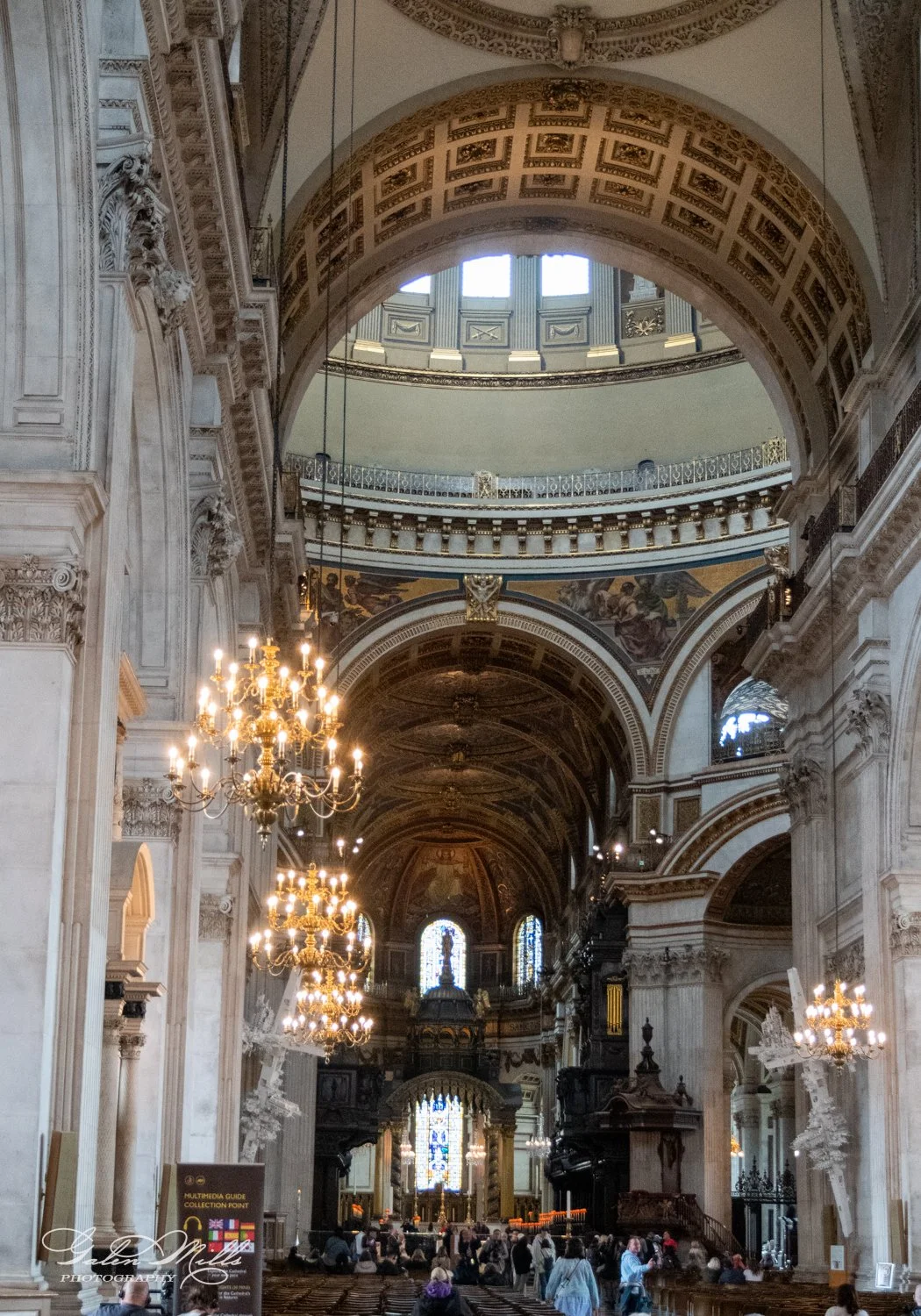 Interior of a grand cathedral with ornate architecture, chandeliers, stained glass windows, and a domed ceiling.