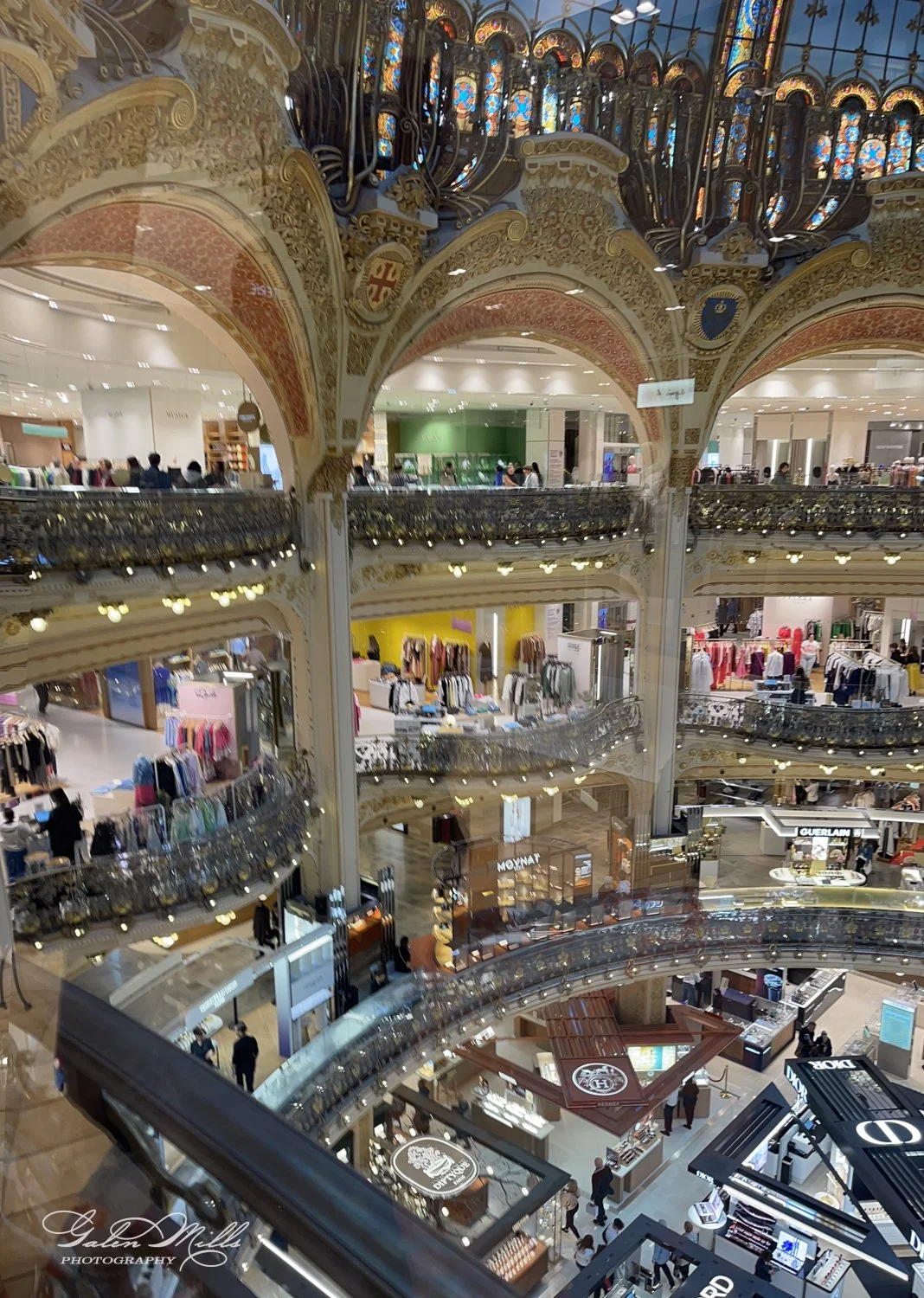 Interior of a luxurious department store with ornate stained glass ceiling and multiple levels of merchandise displays.