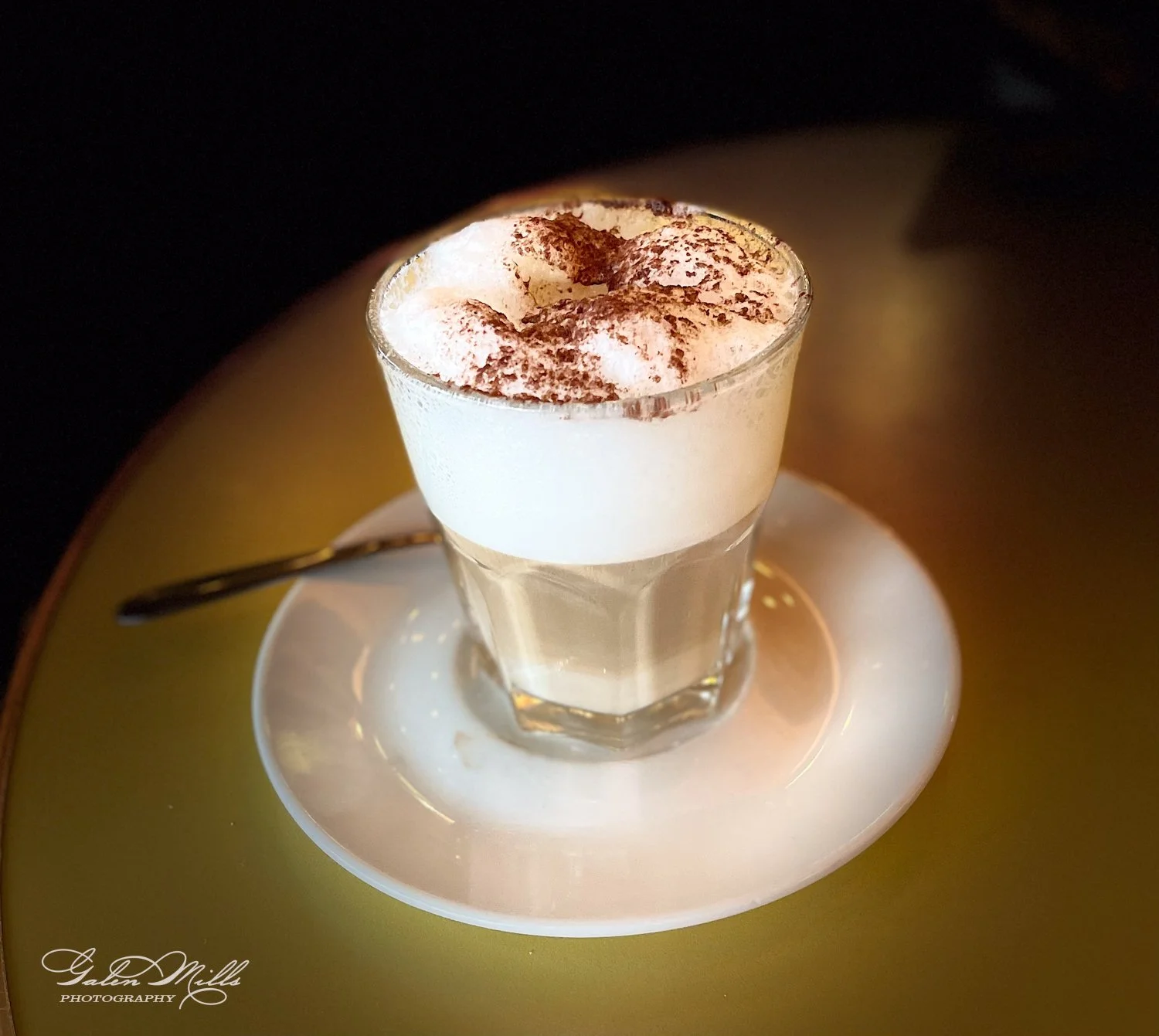 Cappuccino with foam and chocolate sprinkles in a glass cup on a white saucer with a spoon.