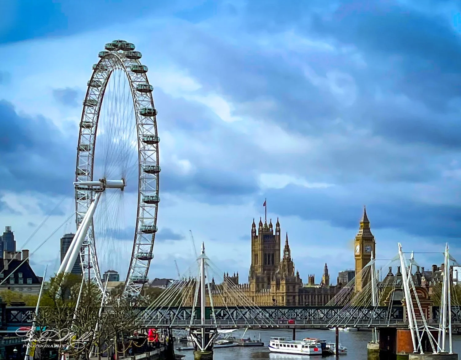 The London Eye, River Thames, and Big Ben in London under a cloudy sky.