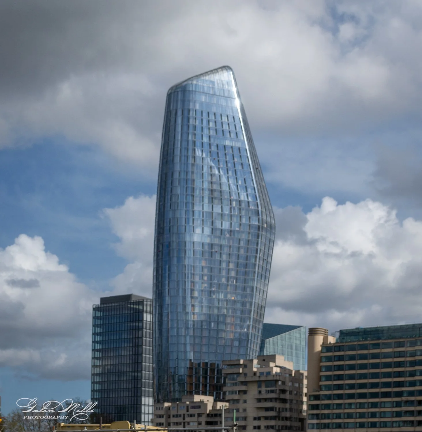 Modern skyscraper with curved glass facade against a cloudy sky.