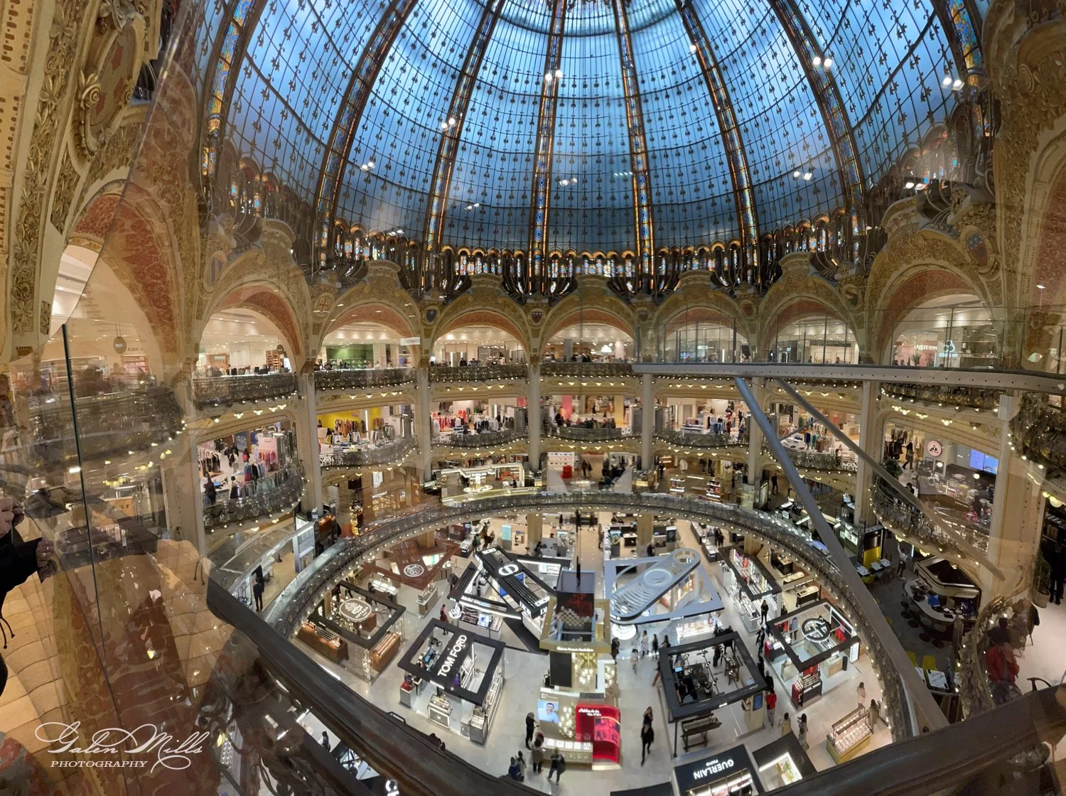 Interior of a large, ornate shopping mall with a glass dome ceiling and multiple levels of stores.