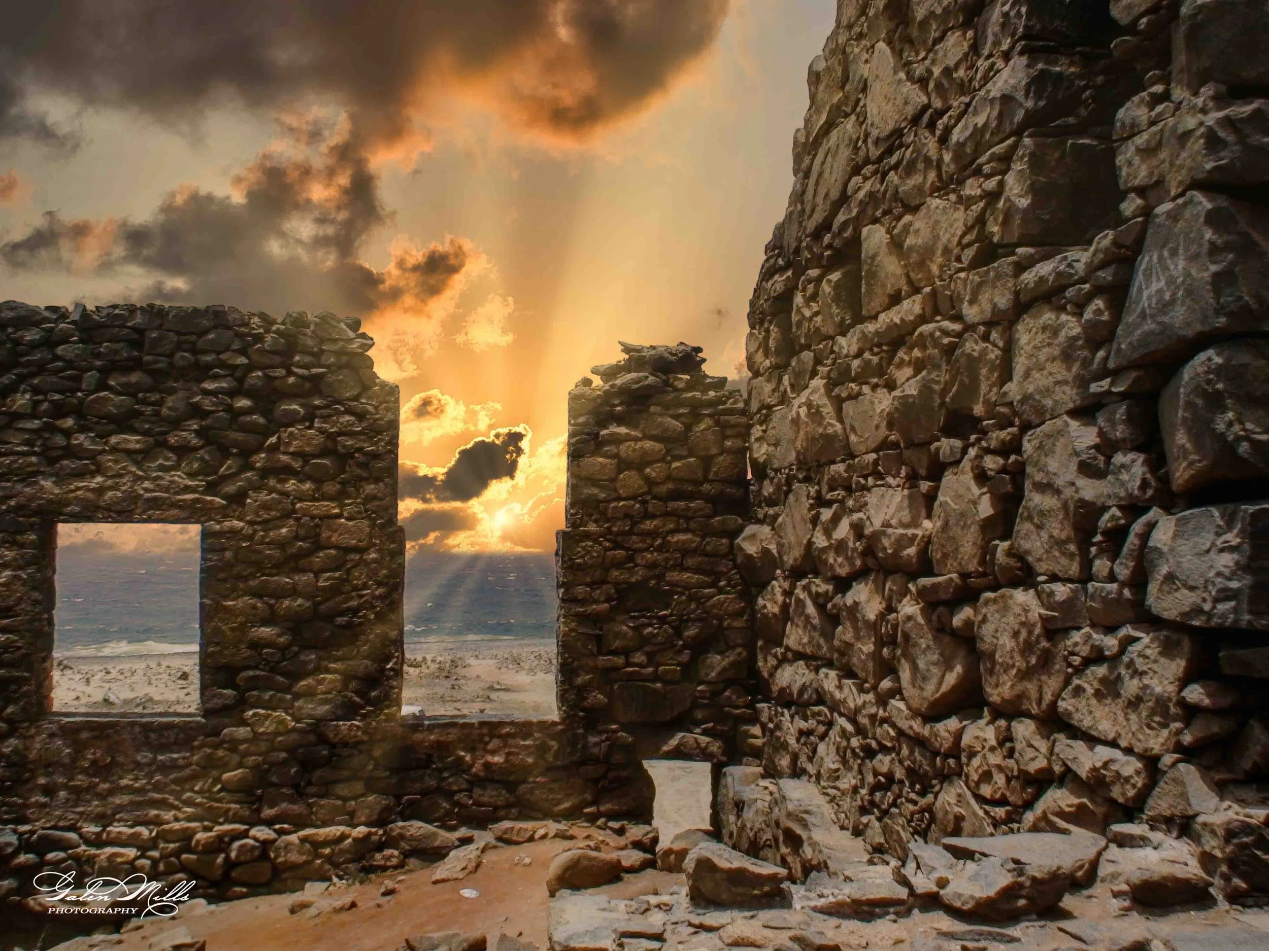 Ruins of an old stone building at sunset with the ocean visible through window openings.