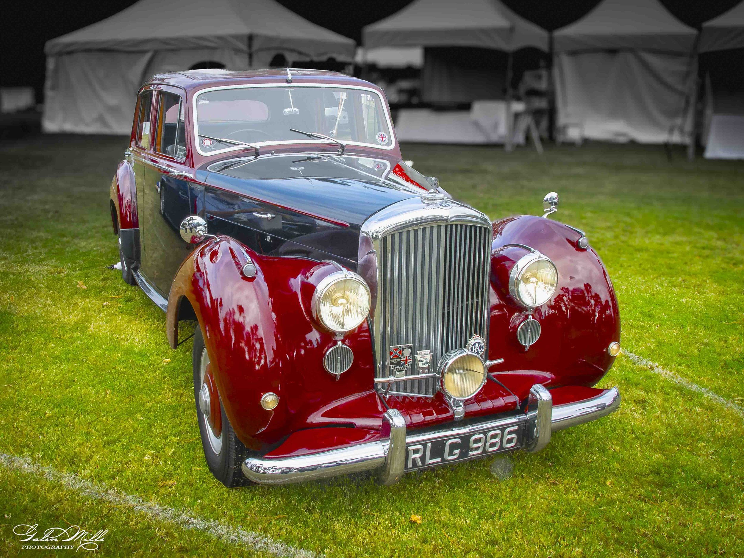 A vintage red and black classic car parked on a grassy field.
