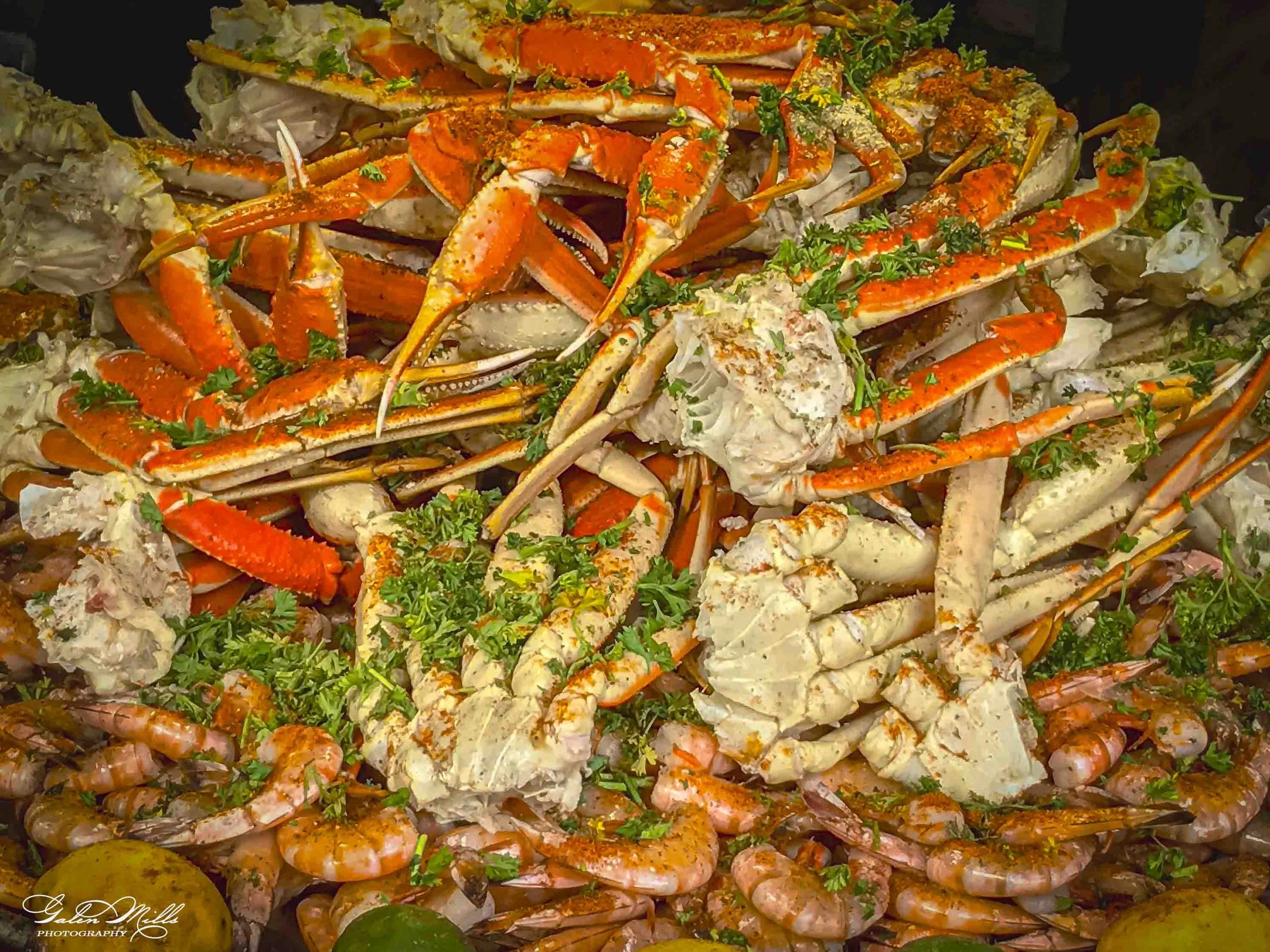 A large pile of cooked crab legs garnished with chopped parsley, arranged on a bed of oyster shells.