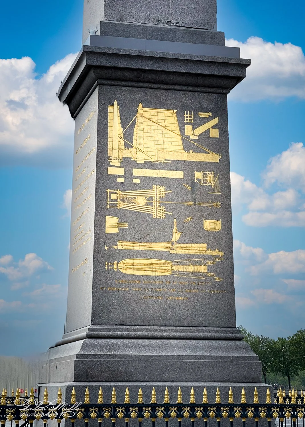 Close-up of a monument pedestal with golden engravings depicting architectural designs against a cloudy sky.