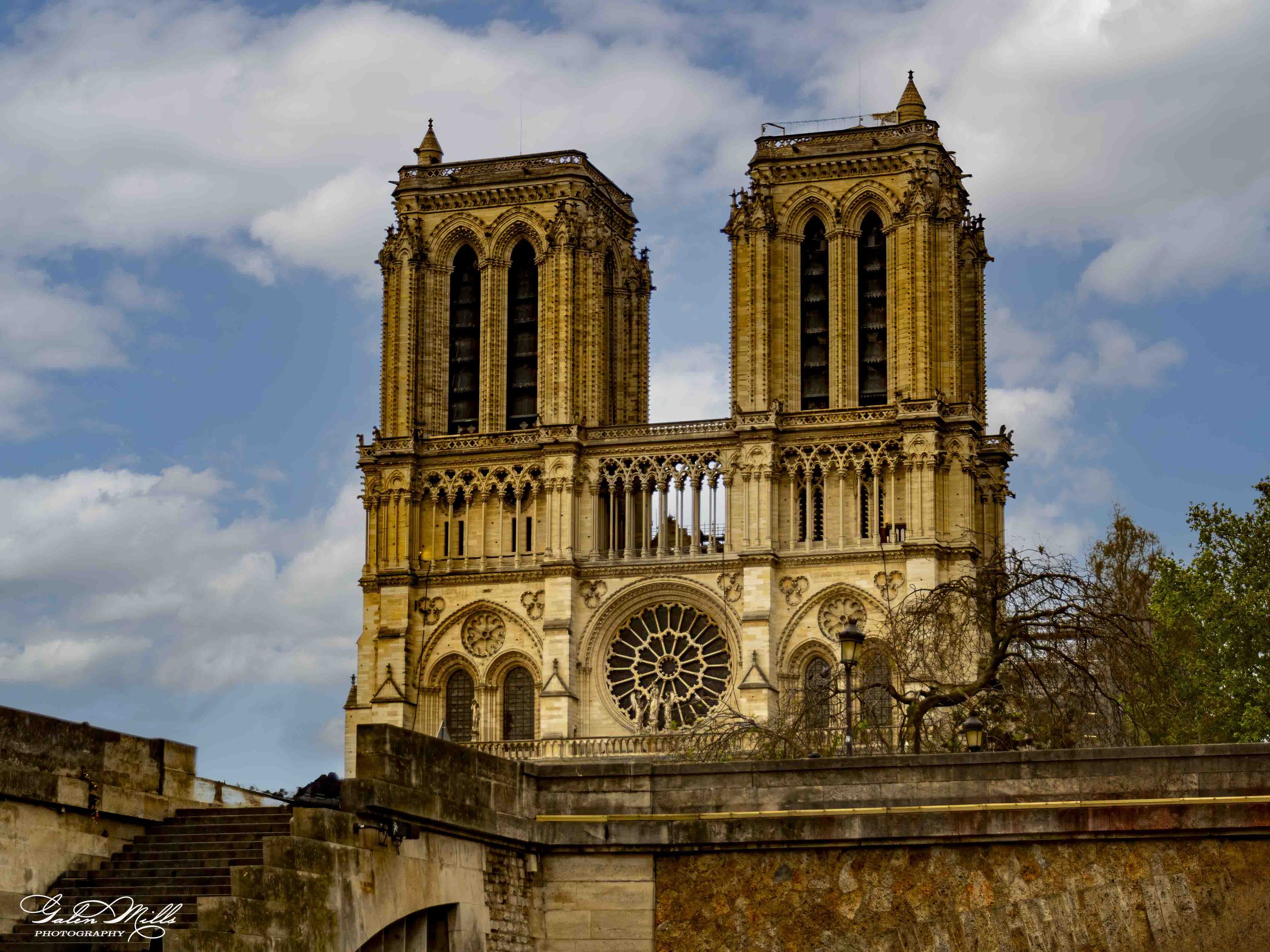 Notre-Dame Cathedral in Paris with twin towers and ornate architecture against a cloudy sky.