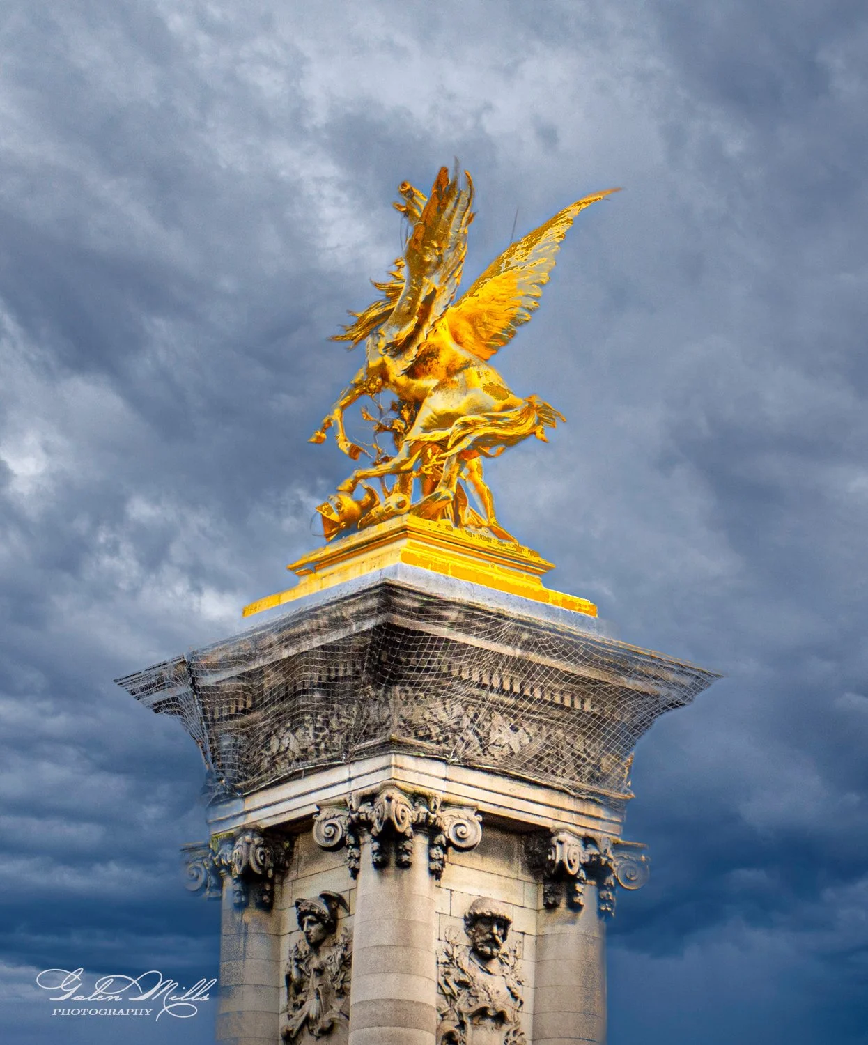 Golden winged horse statue on ornate pillar with cloudy sky