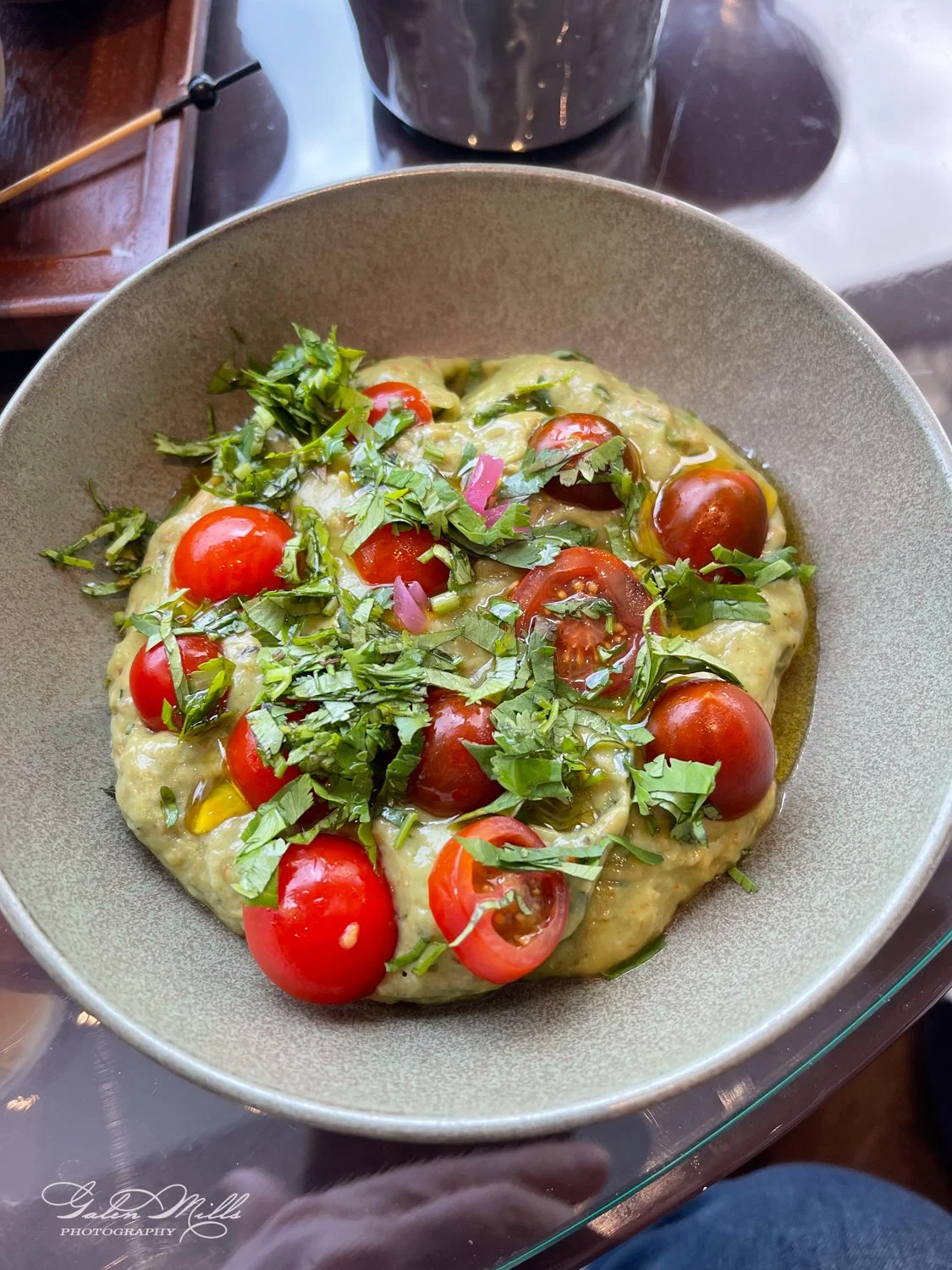 Bowl of guacamole topped with cherry tomatoes, chopped onions, and cilantro.
