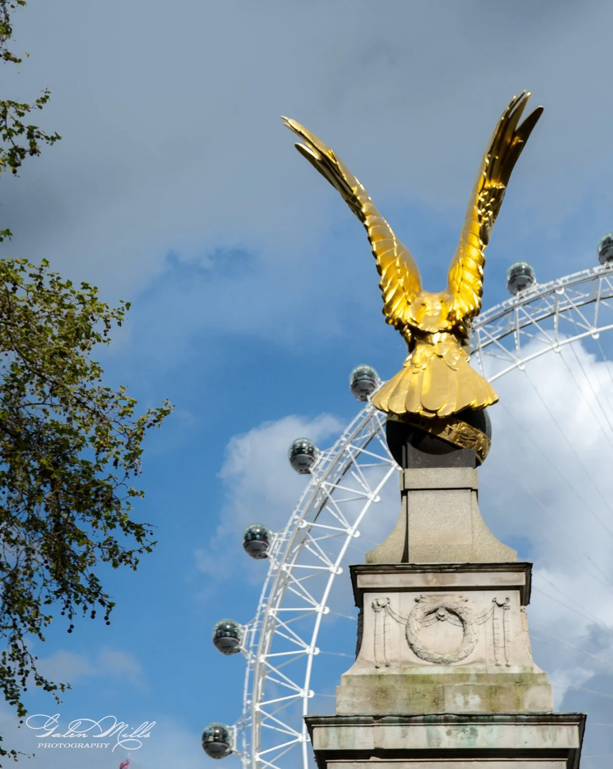 Golden eagle sculpture atop a stone pedestal with a ferris wheel in the background.