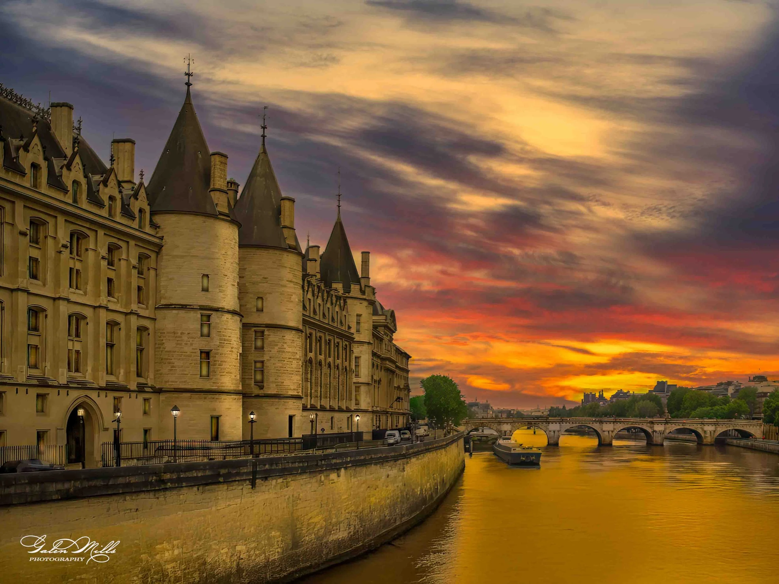 Sunset over the Seine River in Paris with a historic castle-like building, bridge, and boats in the foreground.