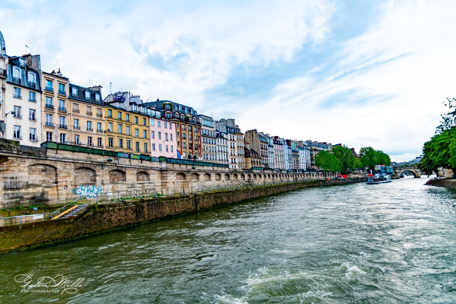 Colorful buildings along the Seine River in Paris, with a boat on the water and an arched bridge in the background.