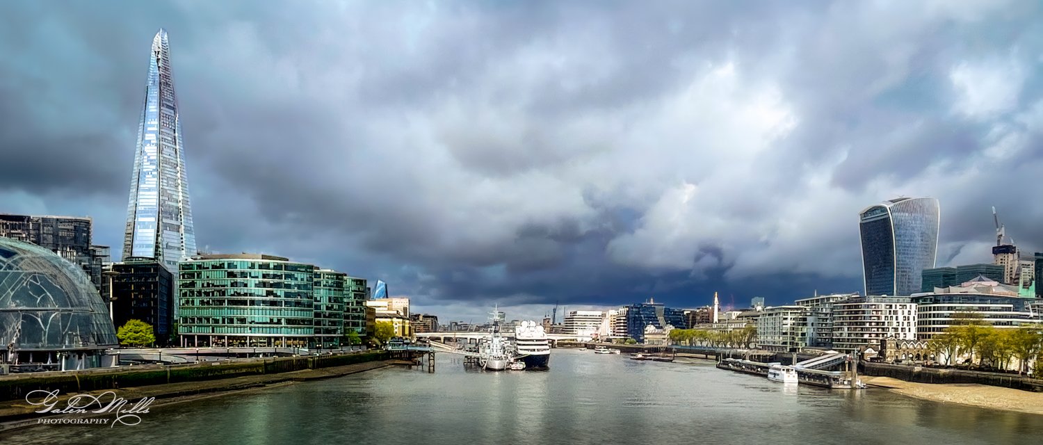 London cityscape featuring The Shard, river Thames, modern buildings, and cloudy sky.