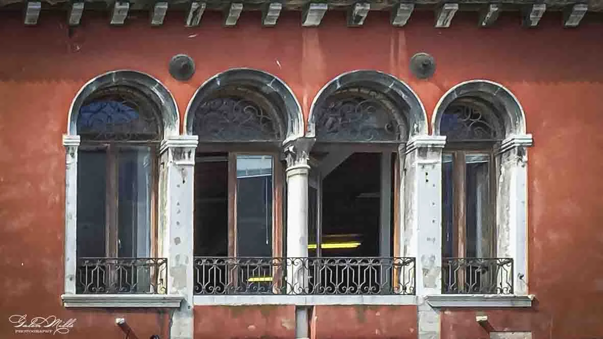 Close-up of a building facade with four arched windows and decorative columns, featuring ornate wrought iron balcony railings.