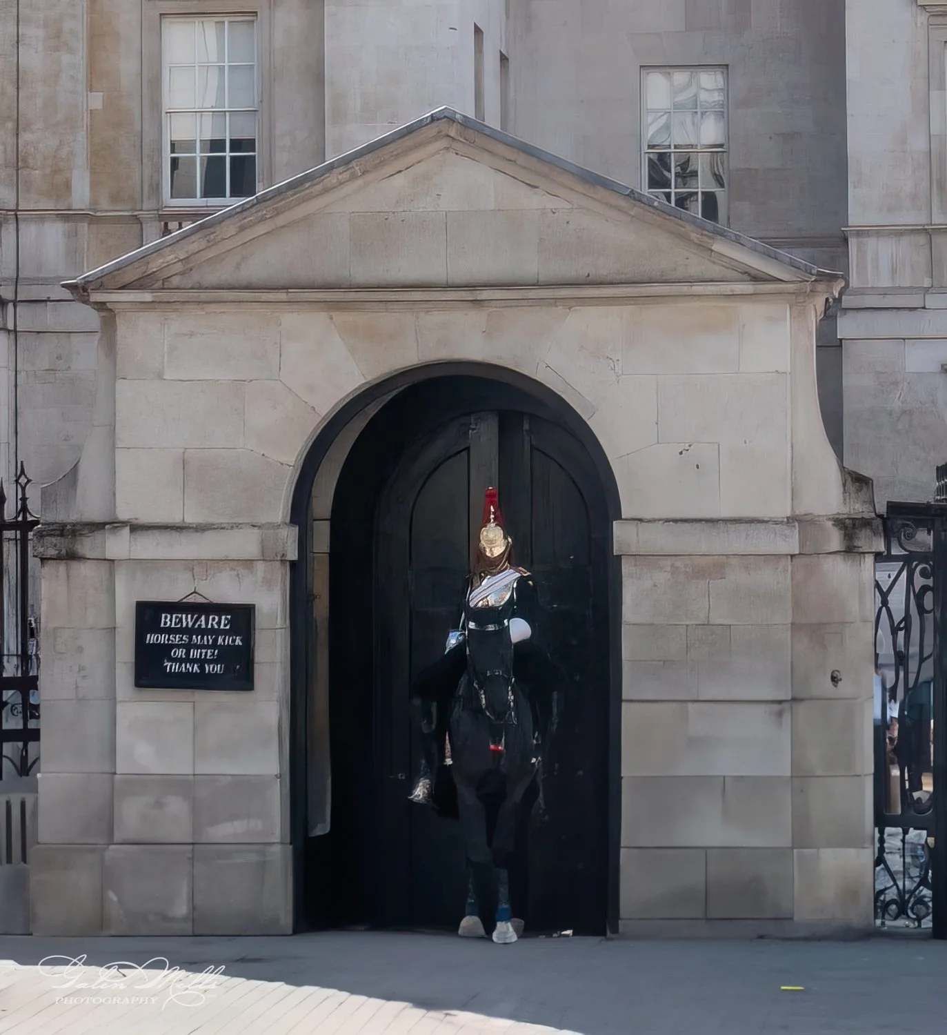 Mounted guard in uniform on horseback at historic building entrance with warning sign.