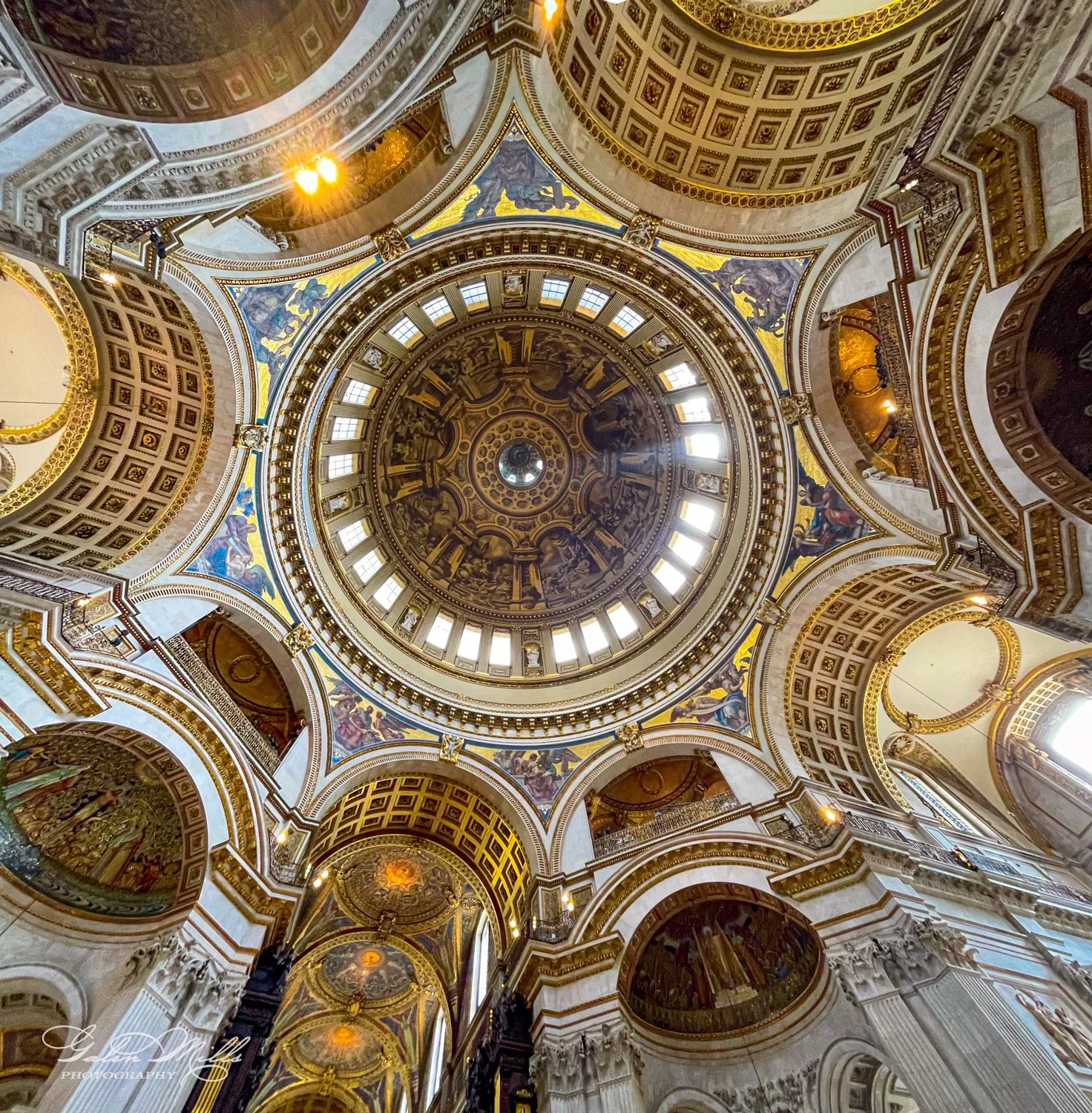 Interior of a grand cathedral dome with intricate architectural details, ornate patterns, and decorative artwork, featuring large windows allowing natural light.