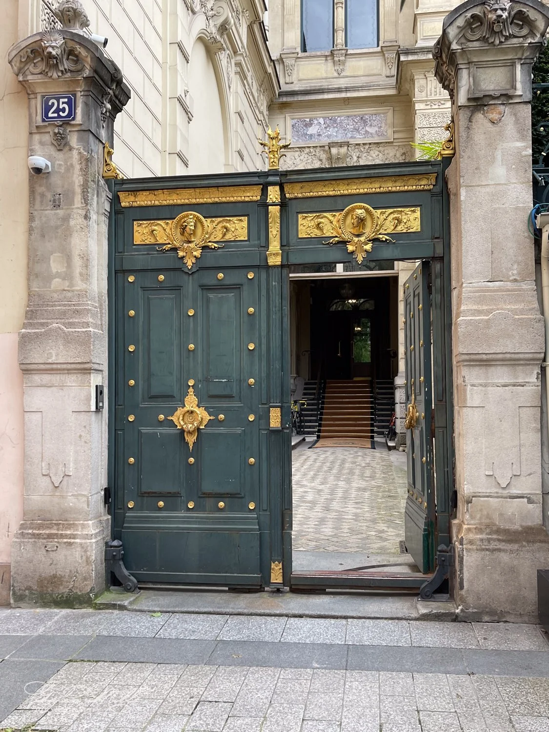 Ornate green and gold gate at entryway of historic building with stone columns and arched architecture.