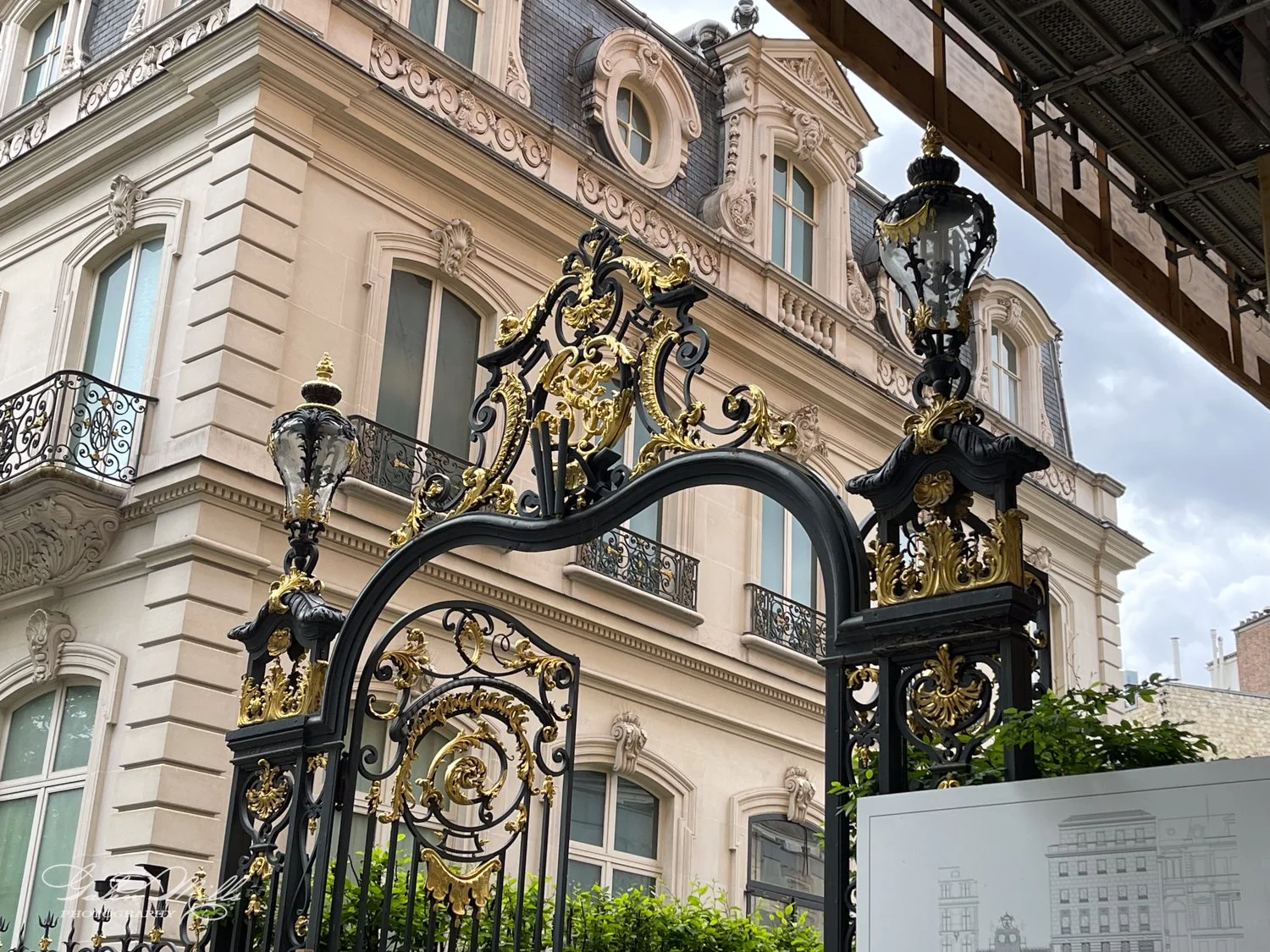 Ornate wrought iron gate with gold details in front of a historic stone building with arched windows and decorative balconies.