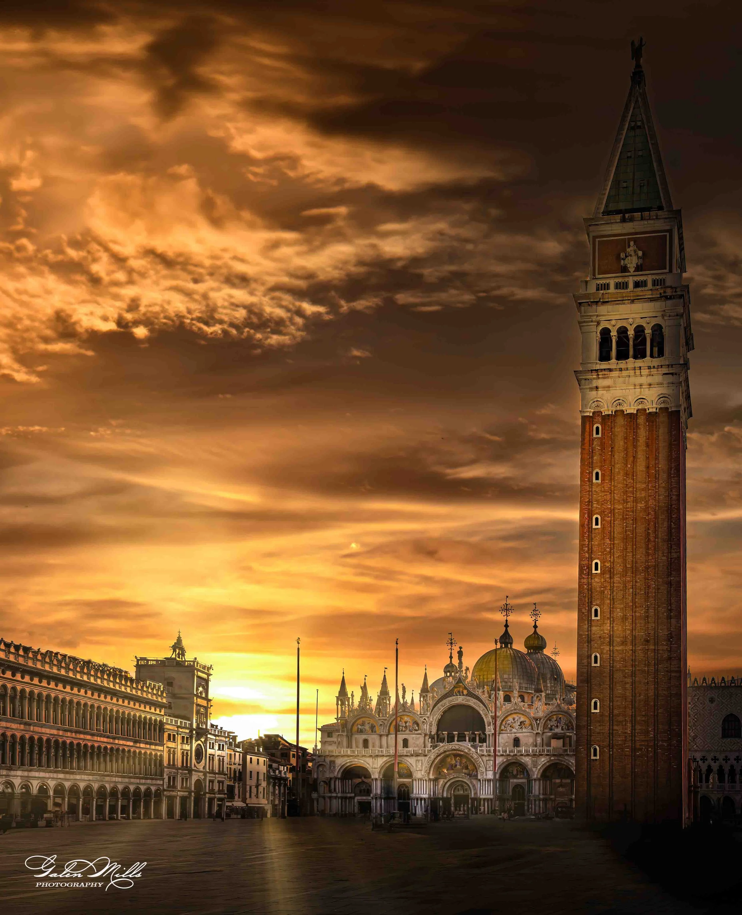 Venetian square at sunset with St. Mark's Basilica, tall bell tower, and surrounding historic buildings under a dramatic cloudy sky.