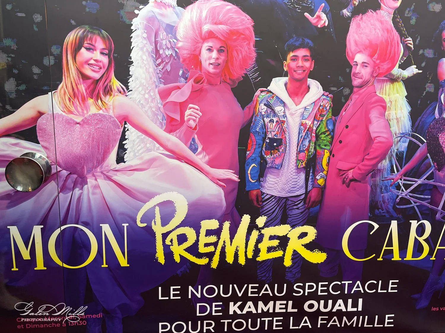 Promotional poster for "Mon Premier Cabaret," a new show by Kamel Ouali. It features performers in colorful costumes, including a woman in a pink dress and two men with pink wigs. The background is dark with vivid colors, highlighting the vibrant the