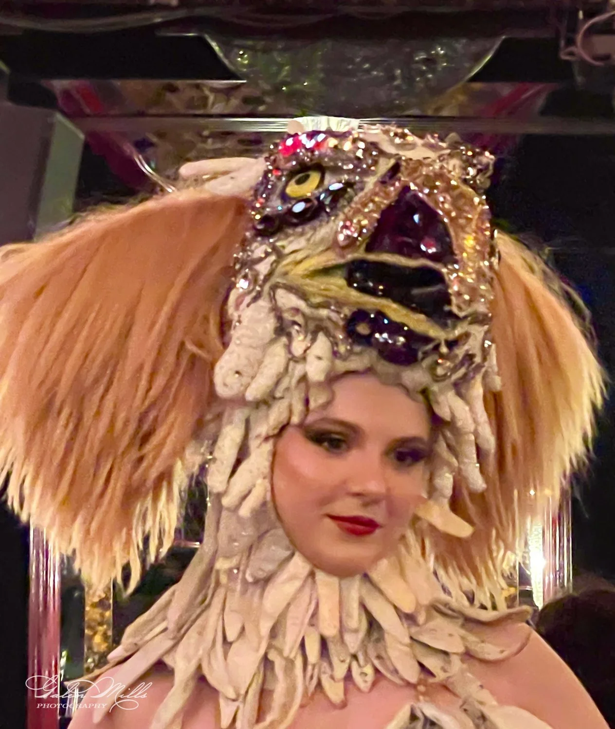 Person wearing an elaborate, artistic headpiece with feathers and jewels, creating a fantastical look.