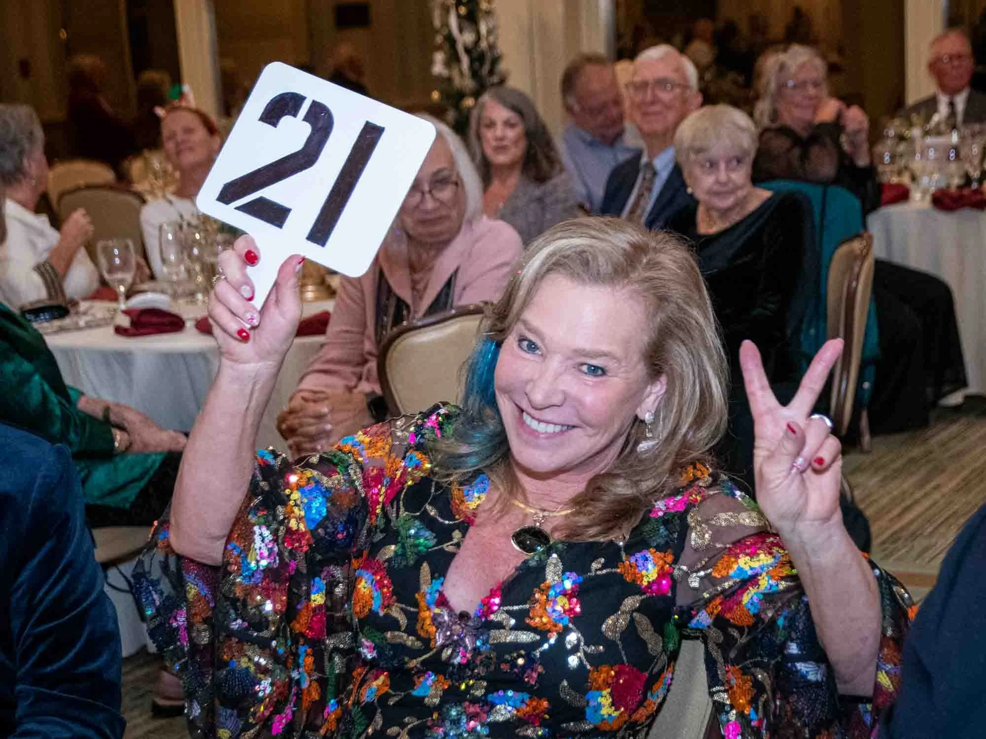 Woman holding a number 21 sign at a formal event, surrounded by seated people.