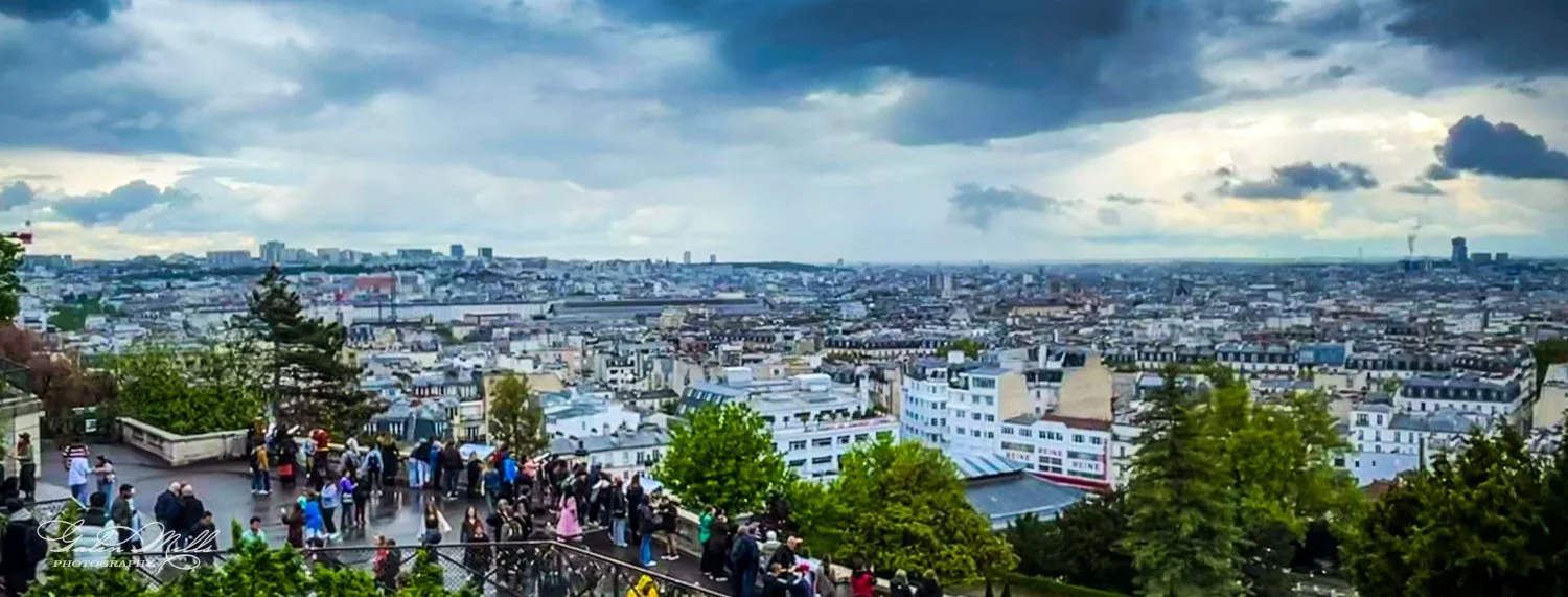 Panoramic view of Paris cityscape with cloudy sky and people at observation point.