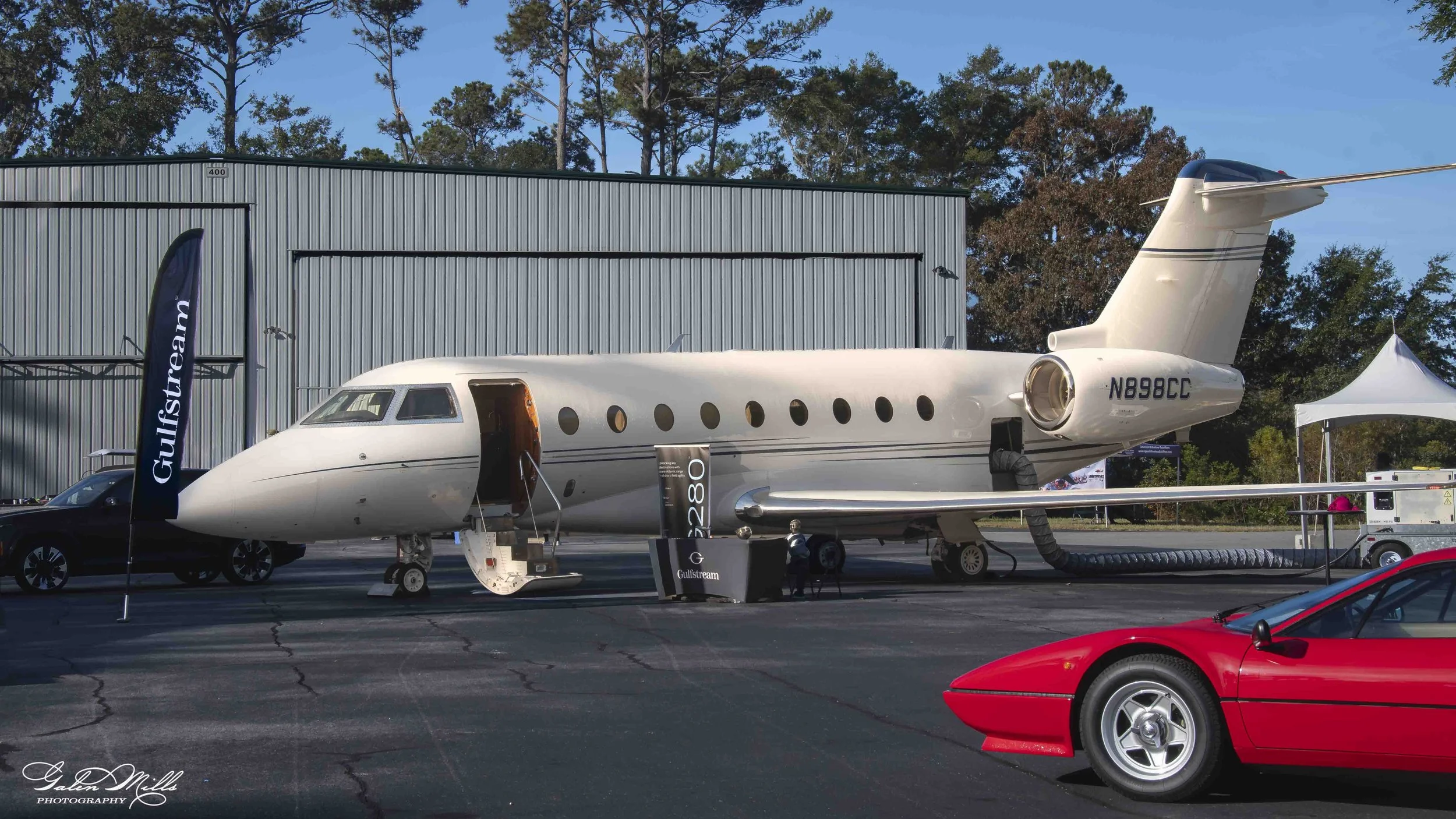 A private jet aircraft parked outdoors surrounded by cars and banners with the Gulfstream logo at an airshow or exhibition event.