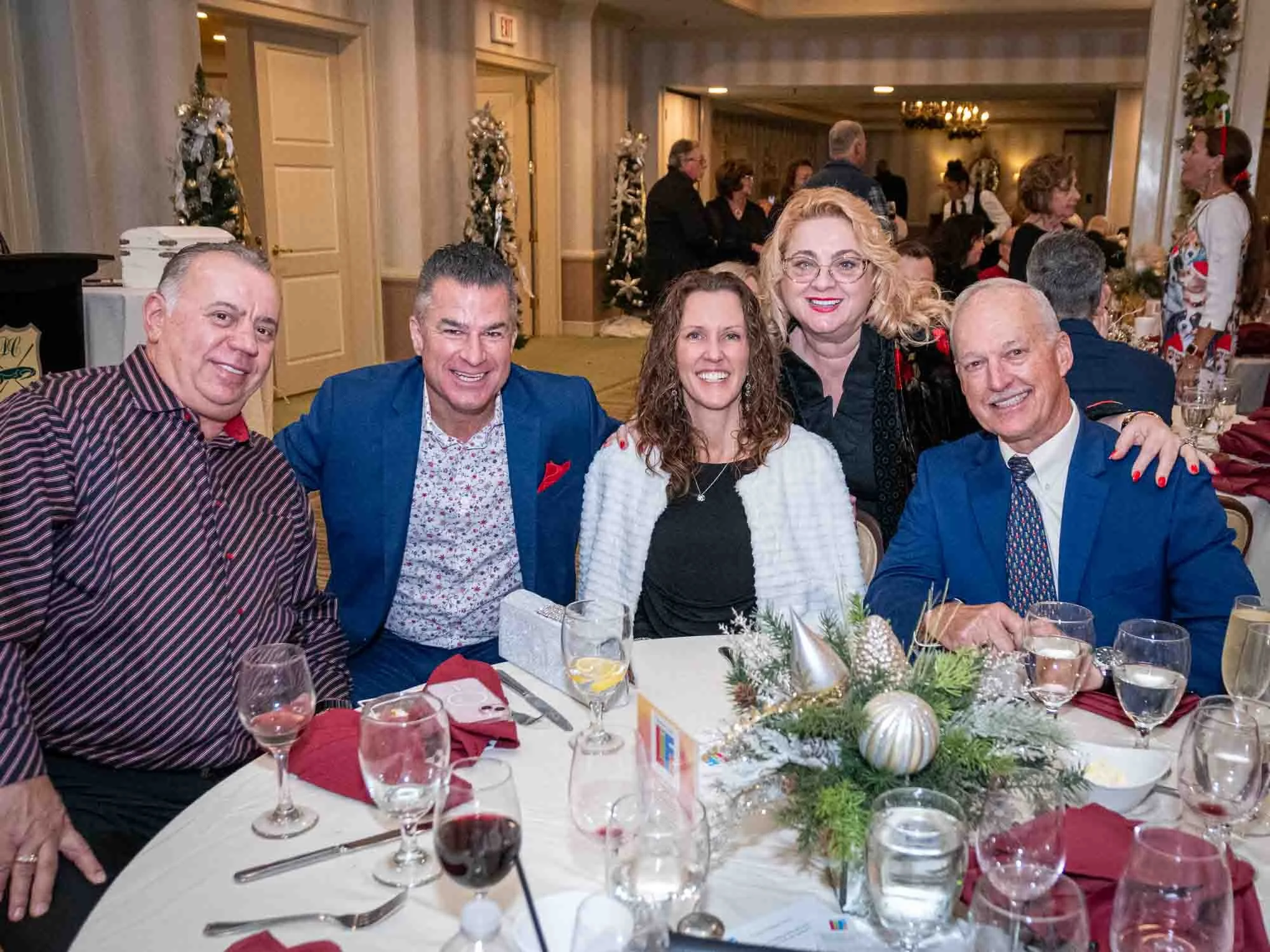 Group of five people seated at a decorated table during a festive event, with holiday decorations and glasses on the table.