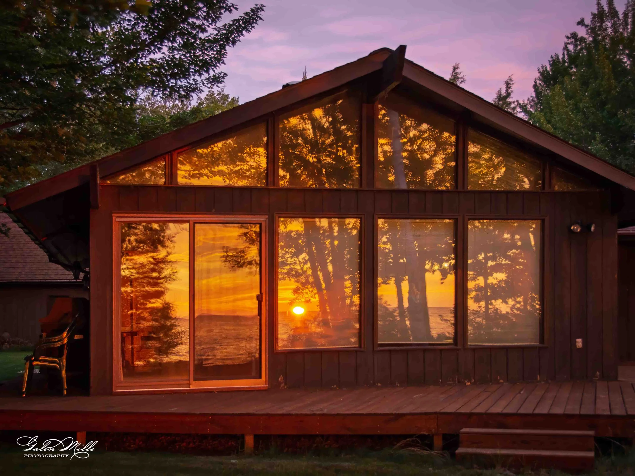Sunset view through the large windows of a wooden house, reflection of trees and colorful sky in the glass.