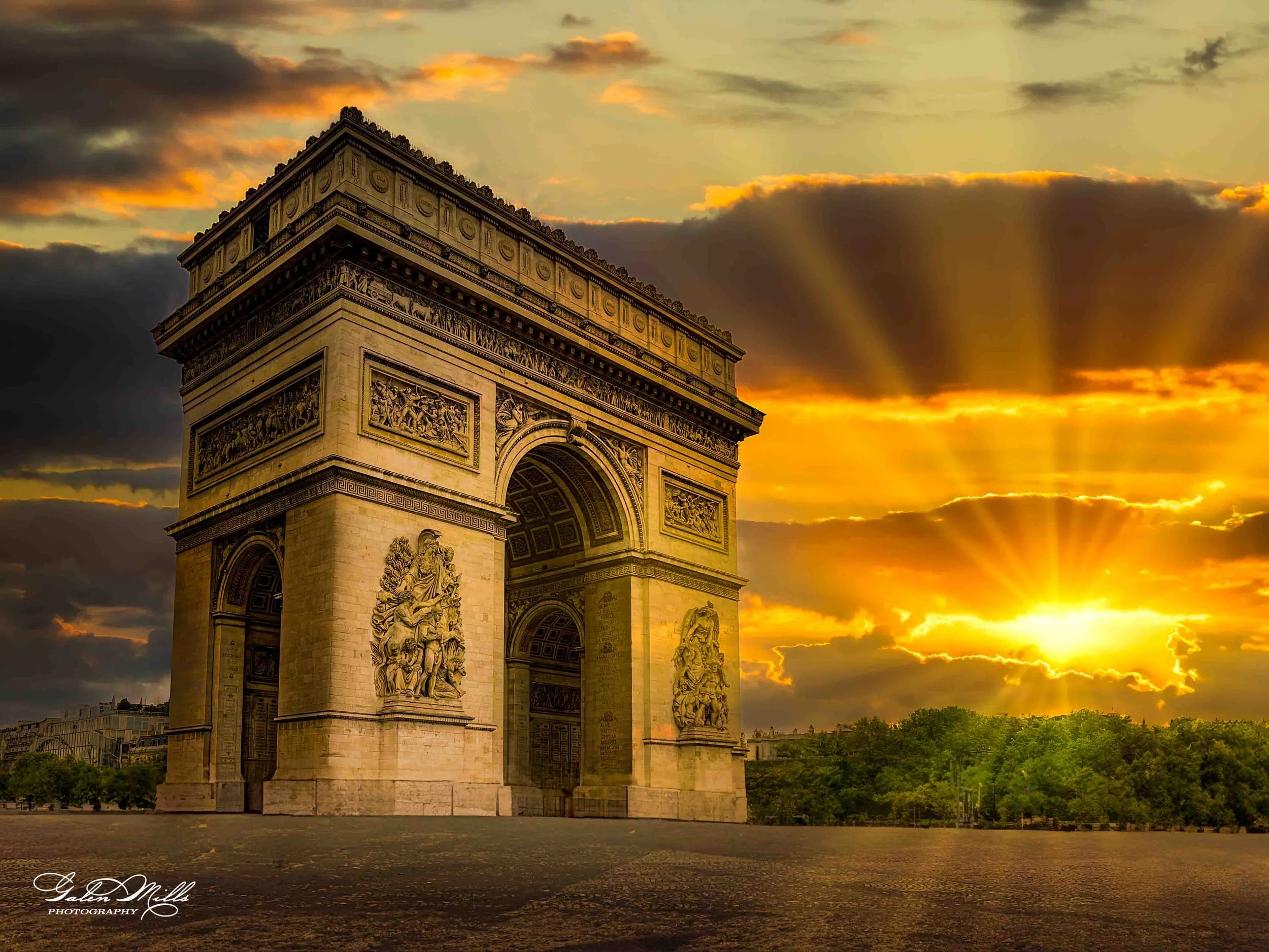 The Arc de Triomphe monument in Paris, France, illuminated by a sunset with clouds and rays of sunlight.