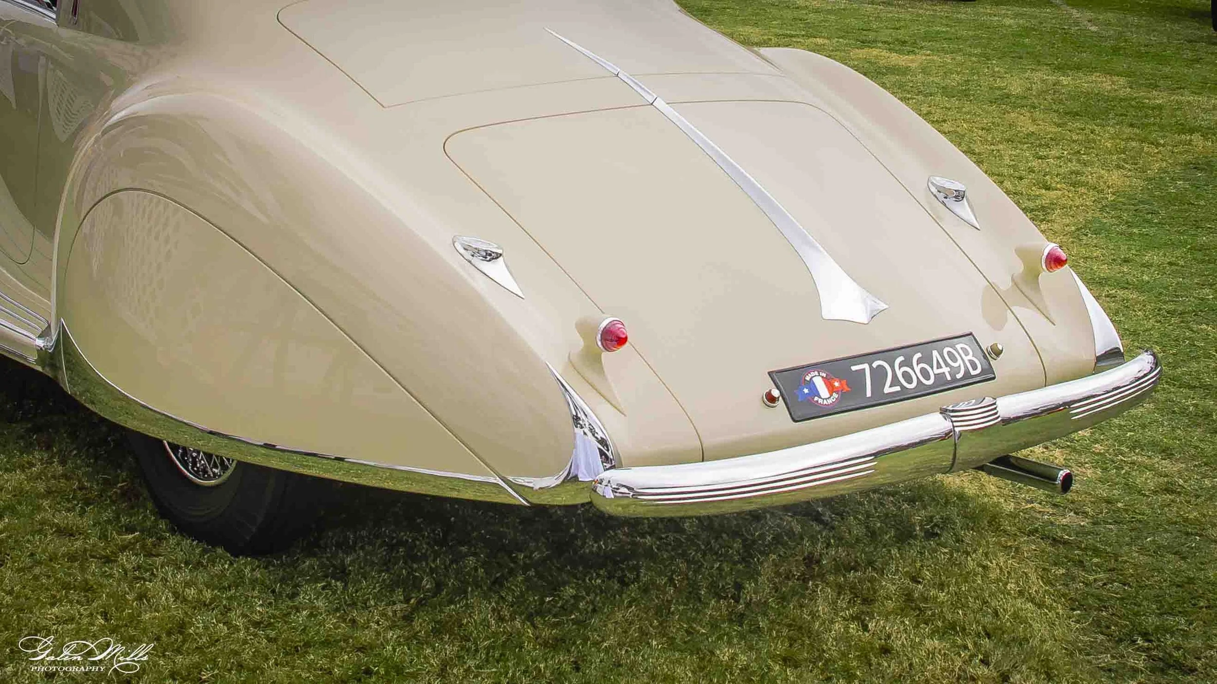 A vintage beige car with a French license plate, parked on grass, with a distinctive rounded body and chrome accents.
