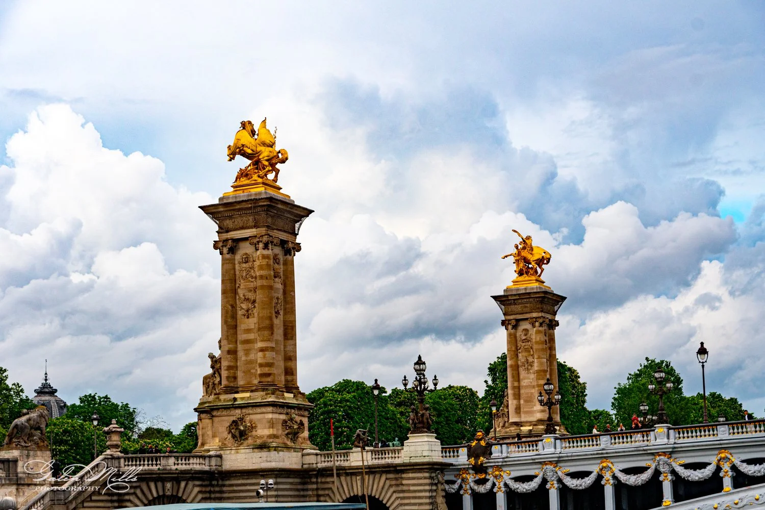 Pont Alexandre III bridge in Paris with golden sculptures and ornate pillars against a cloudy sky.