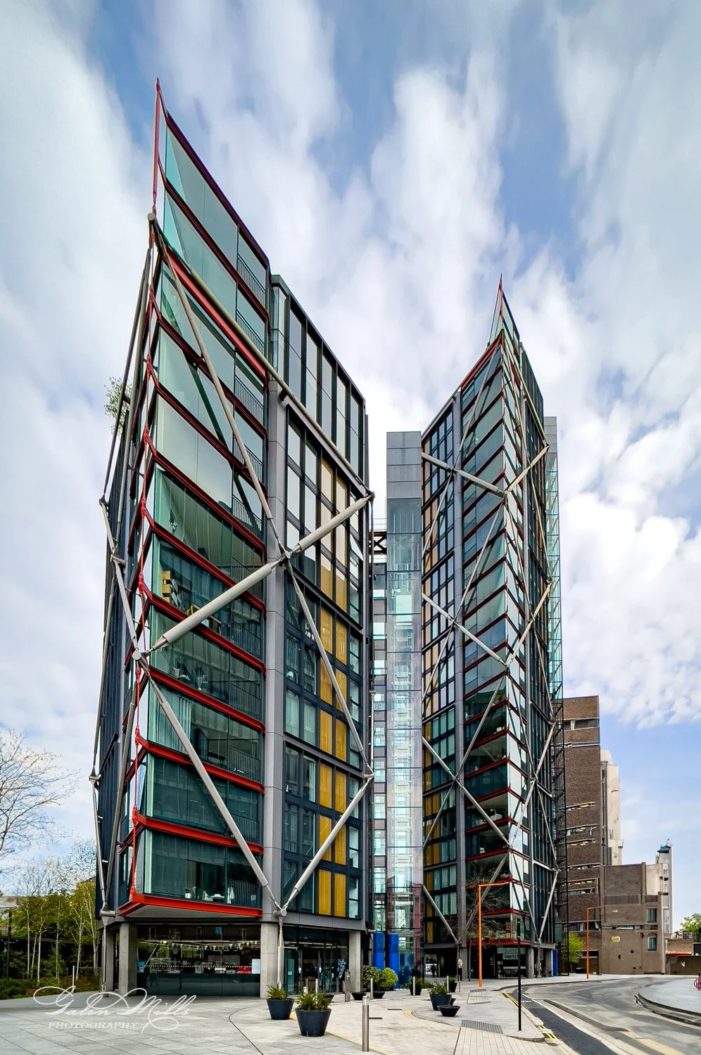 Modern high-rise building with glass and steel facade, featuring colorful panels and exterior cross-bracing, under a partly cloudy sky.