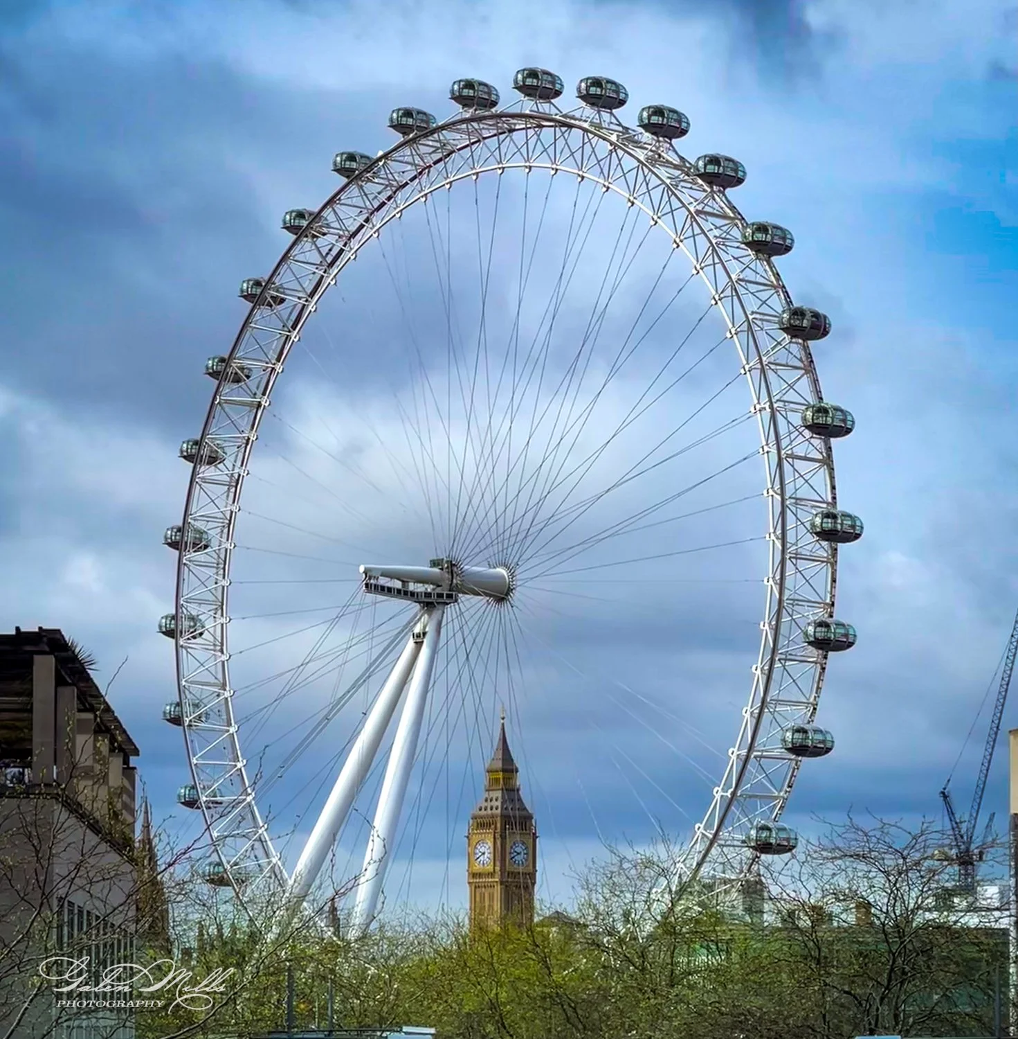 Large Ferris wheel with clock tower in background against cloudy sky.
