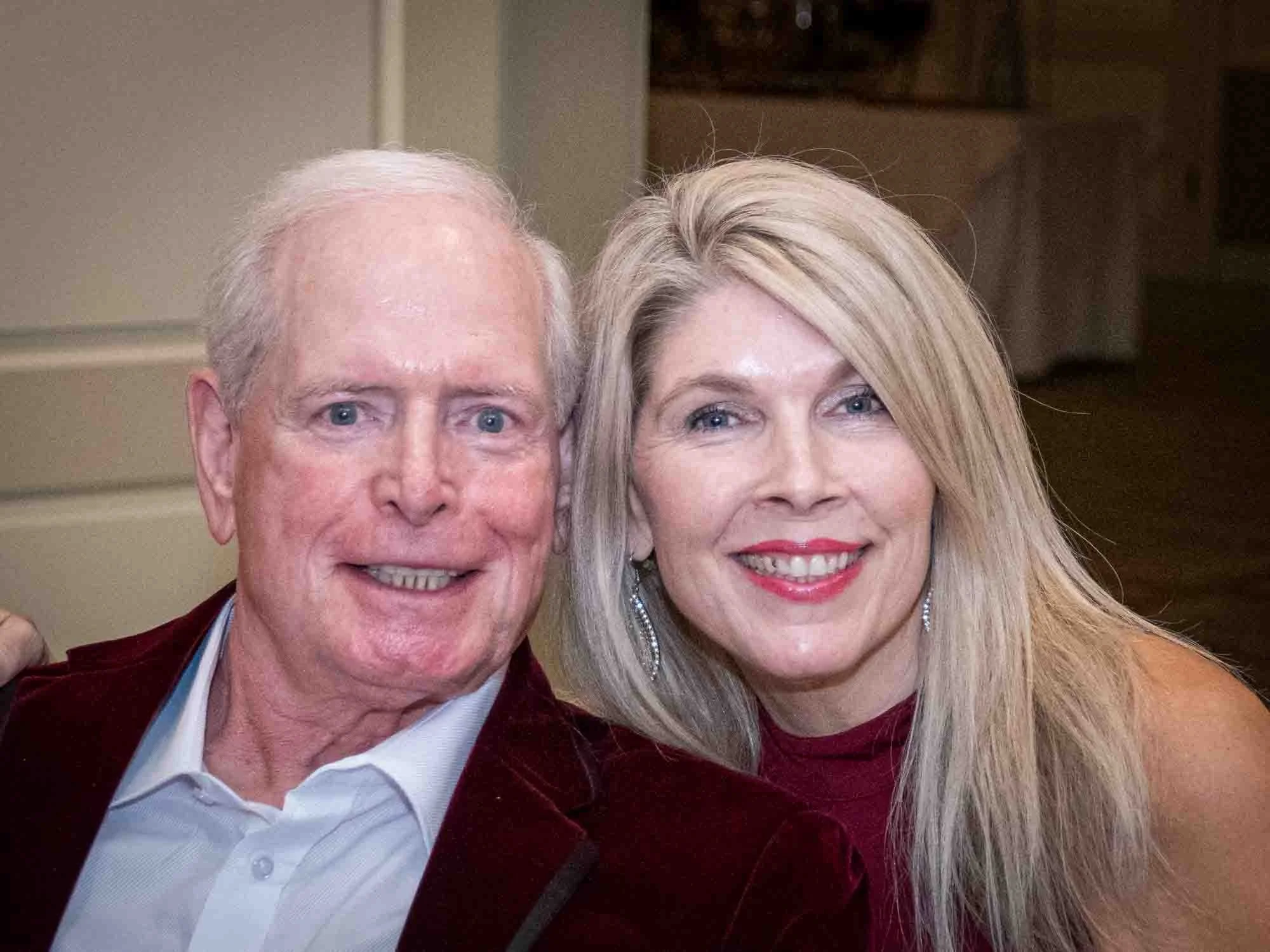 Older couple posing together indoors, smiling.