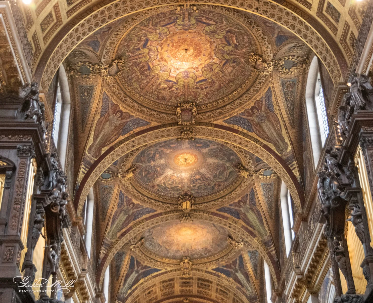 Intricately decorated vaulted ceiling with religious frescoes and ornate designs in a church or cathedral, featuring angelic figures and decorative arches.
