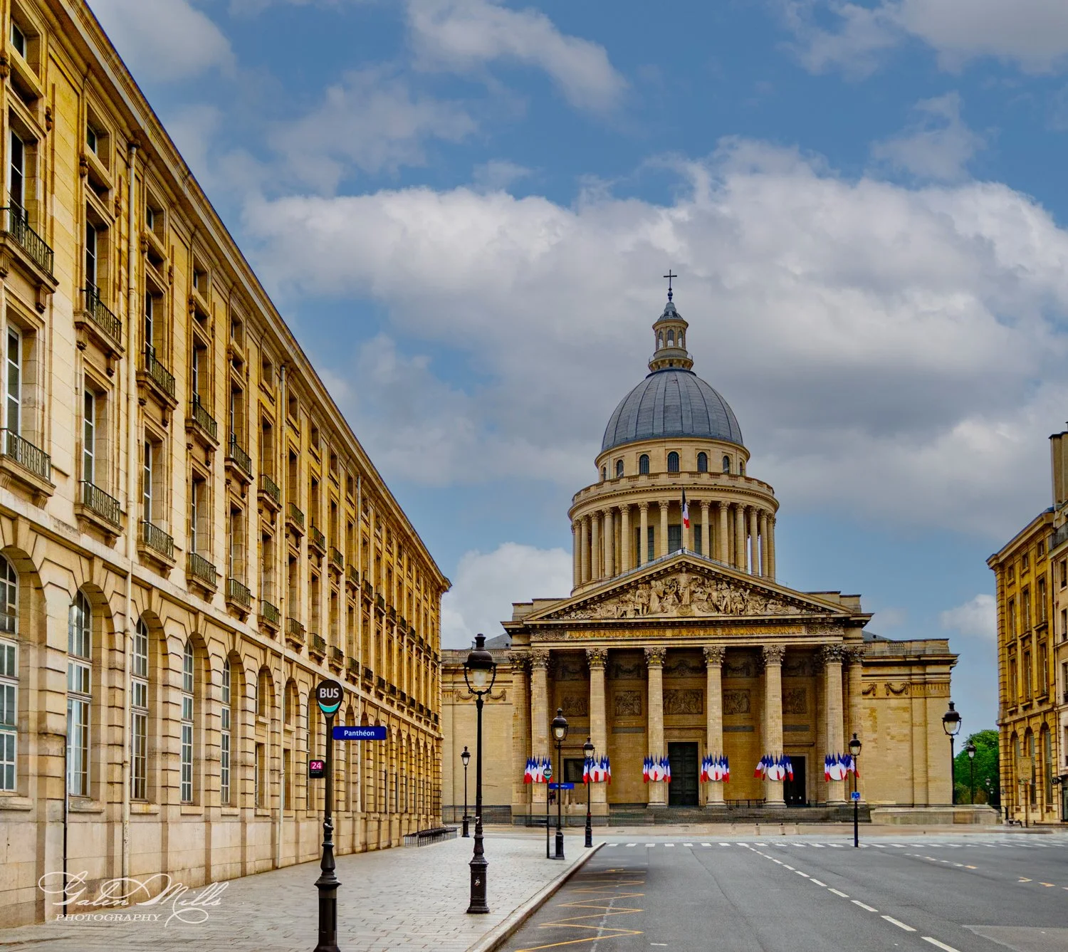 The Pantheon in Paris, France, with classical architecture featuring columns and a large dome, surrounded by buildings and city street with a bus stop sign.