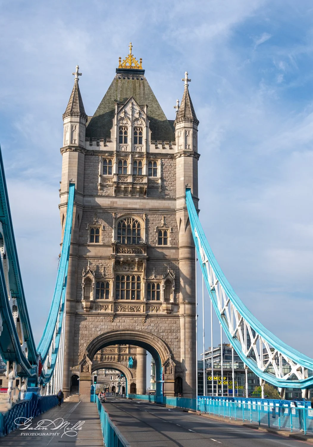 Tower Bridge in London with blue suspension cables and a central stone tower under a clear sky.