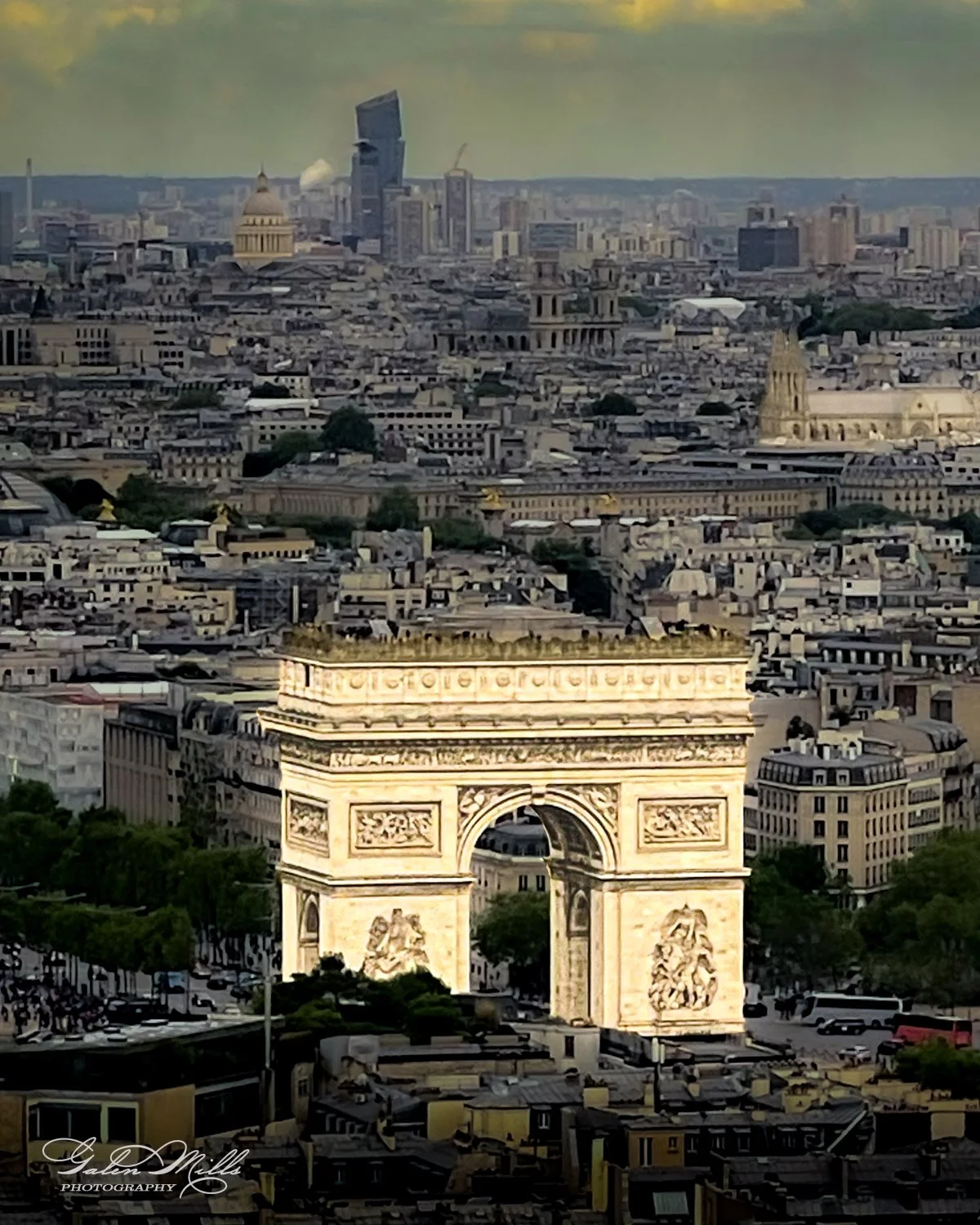 Aerial view of the Arc de Triomphe in Paris, France, with surrounding cityscape and modern buildings in the background.