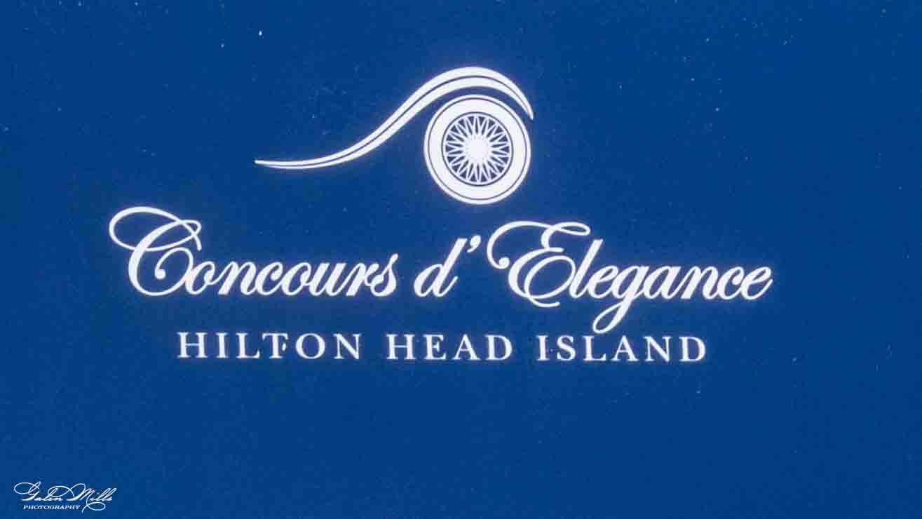 Blue background with white text and logo for the Concours d'Elégance at Hilton Head Island. The logo features a stylized wheel and a swooping line.