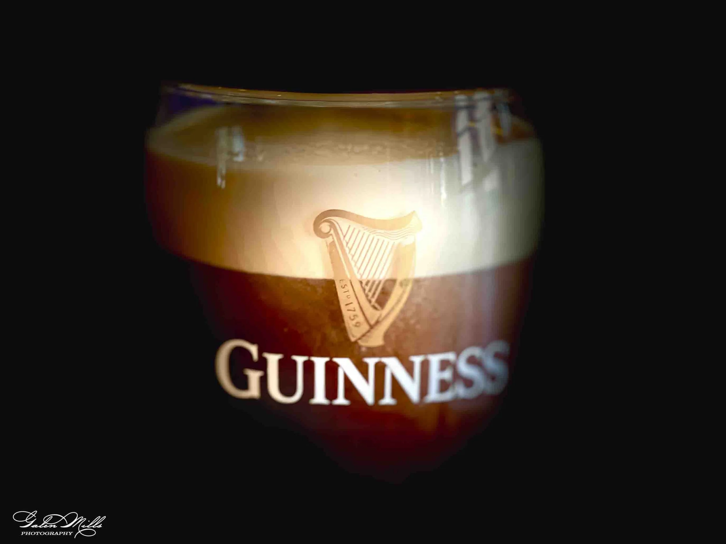 Close-up of a Guinness beer glass with the Guinness logo illuminated.