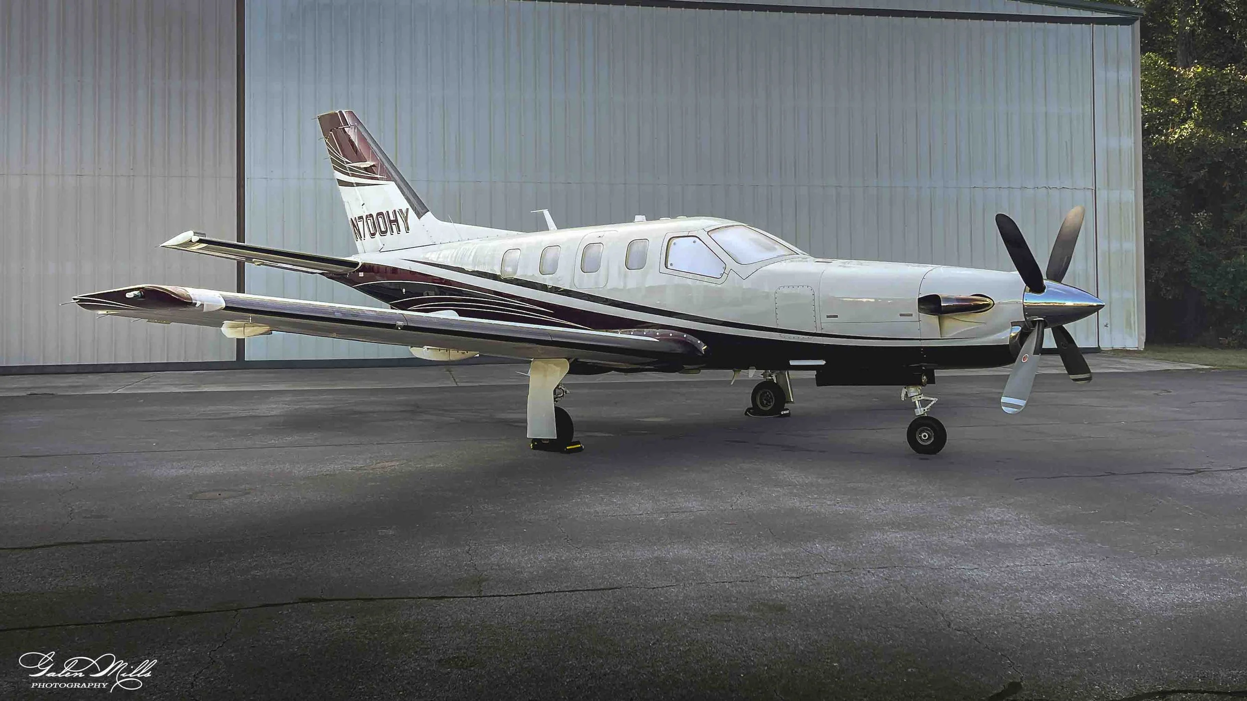 A small white and black private jet airplane parked outdoors on a tarmac with a metal hangar in the background.