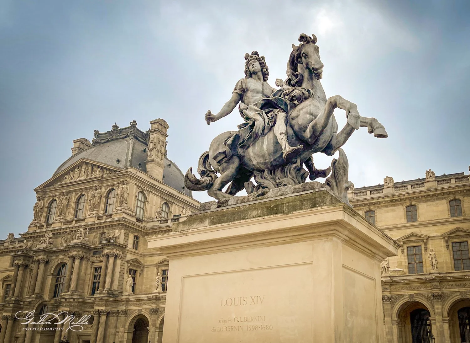 Statue of Louis XIV on horseback outside the Louvre Museum, Paris, with ornate architecture in the background.