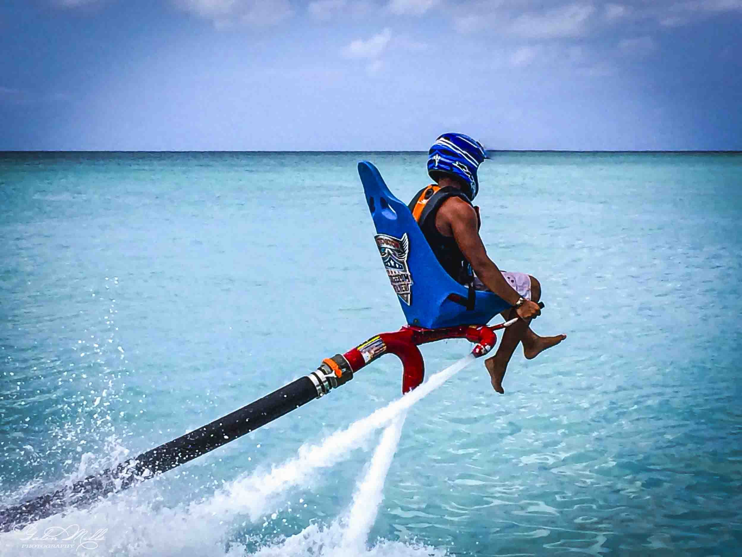 Person windsurfing on calm turquoise ocean under a partly cloudy sky.