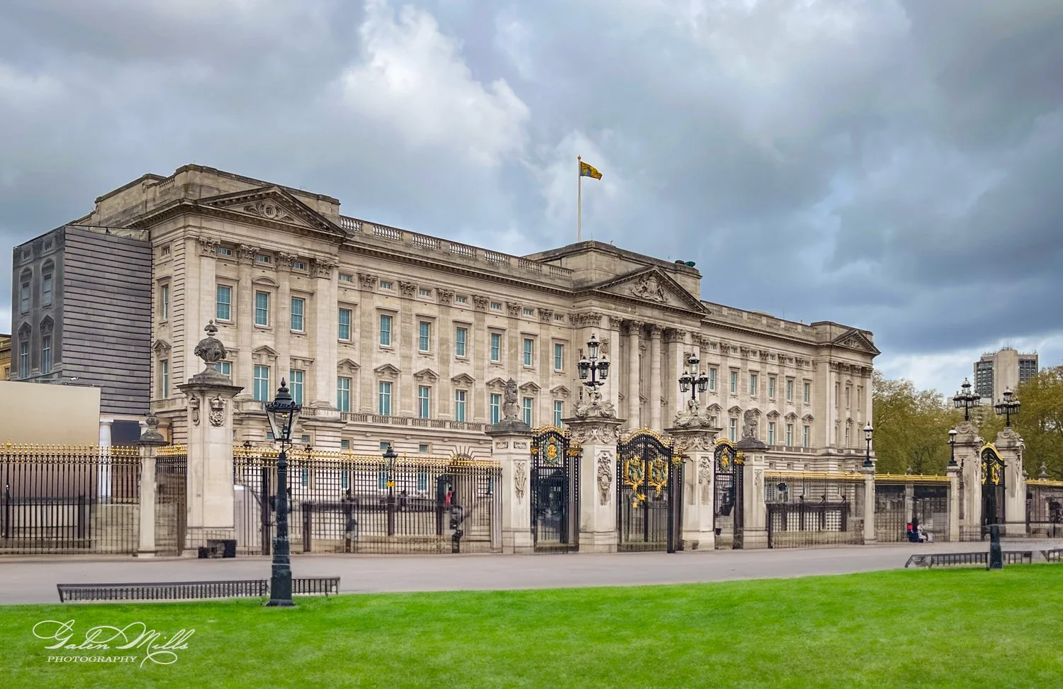 Buckingham Palace in London with ornate gates and a flag on a cloudy day.