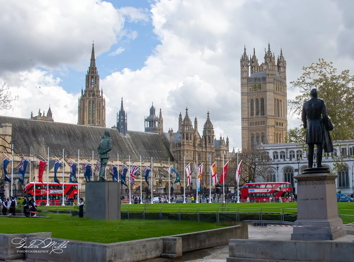 View of the Palace of Westminster, London, with statues, flags, and red double-decker buses.