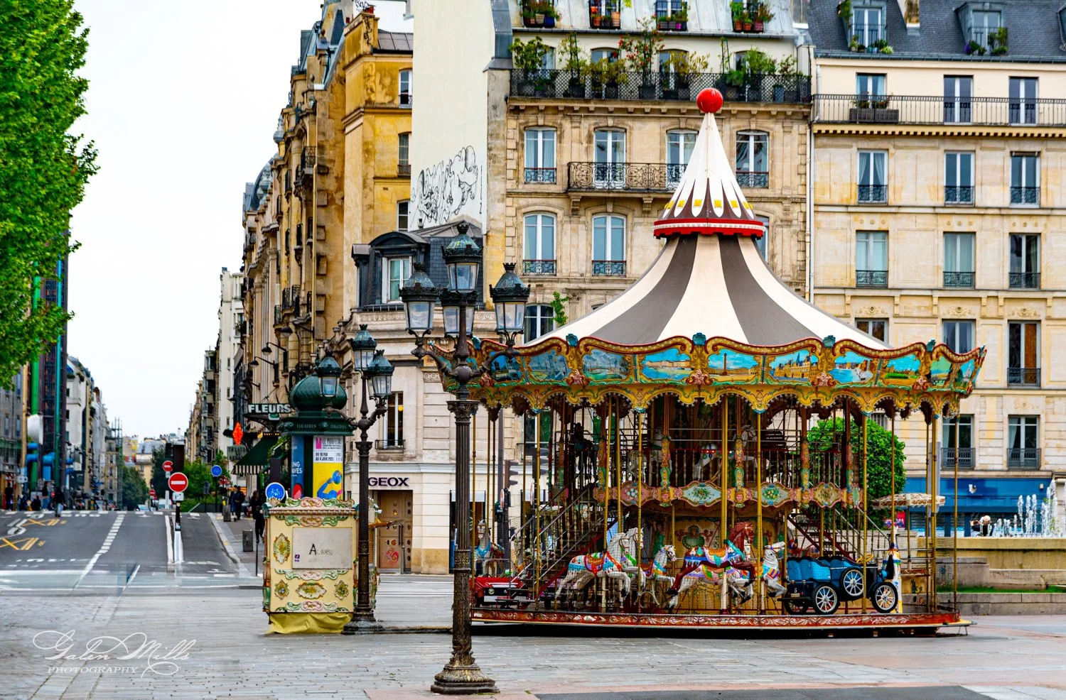 Colorful carousel with horses and a vintage car in a European city square, surrounded by historic buildings with classic architecture.