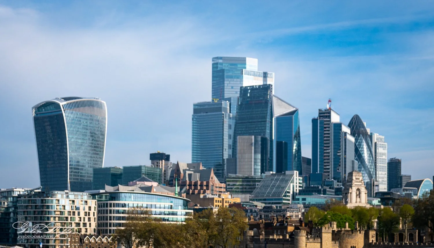 London skyline featuring modern skyscrapers, including the Walkie Talkie and The Gherkin, with clear blue skies.
